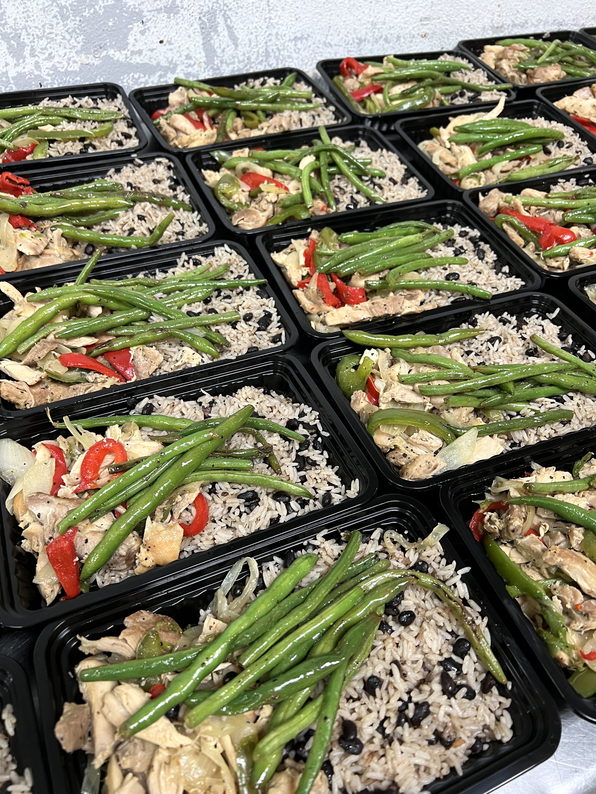 Multiple meal prep containers filled with seasoned rice, grilled chicken, green beans, and sliced red bell peppers.