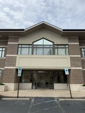 Facade of a commercial building with brick walls, large windows, and two accessible parking signs in front.