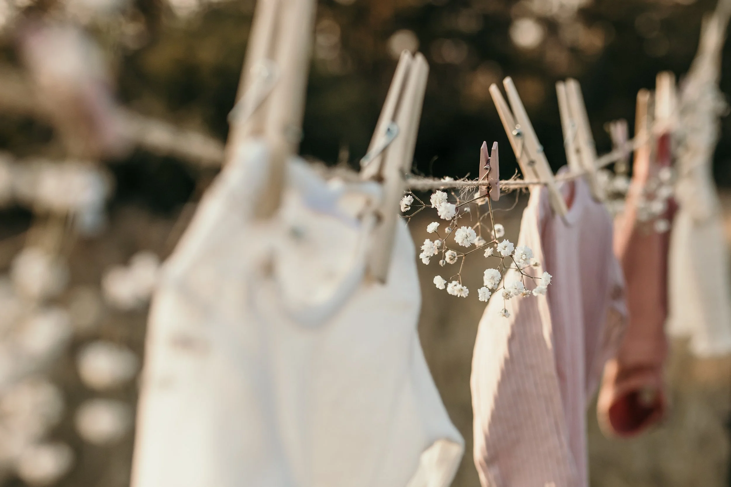 Clothes hanging on a line with clothespins, some with flowers attached, outdoors.