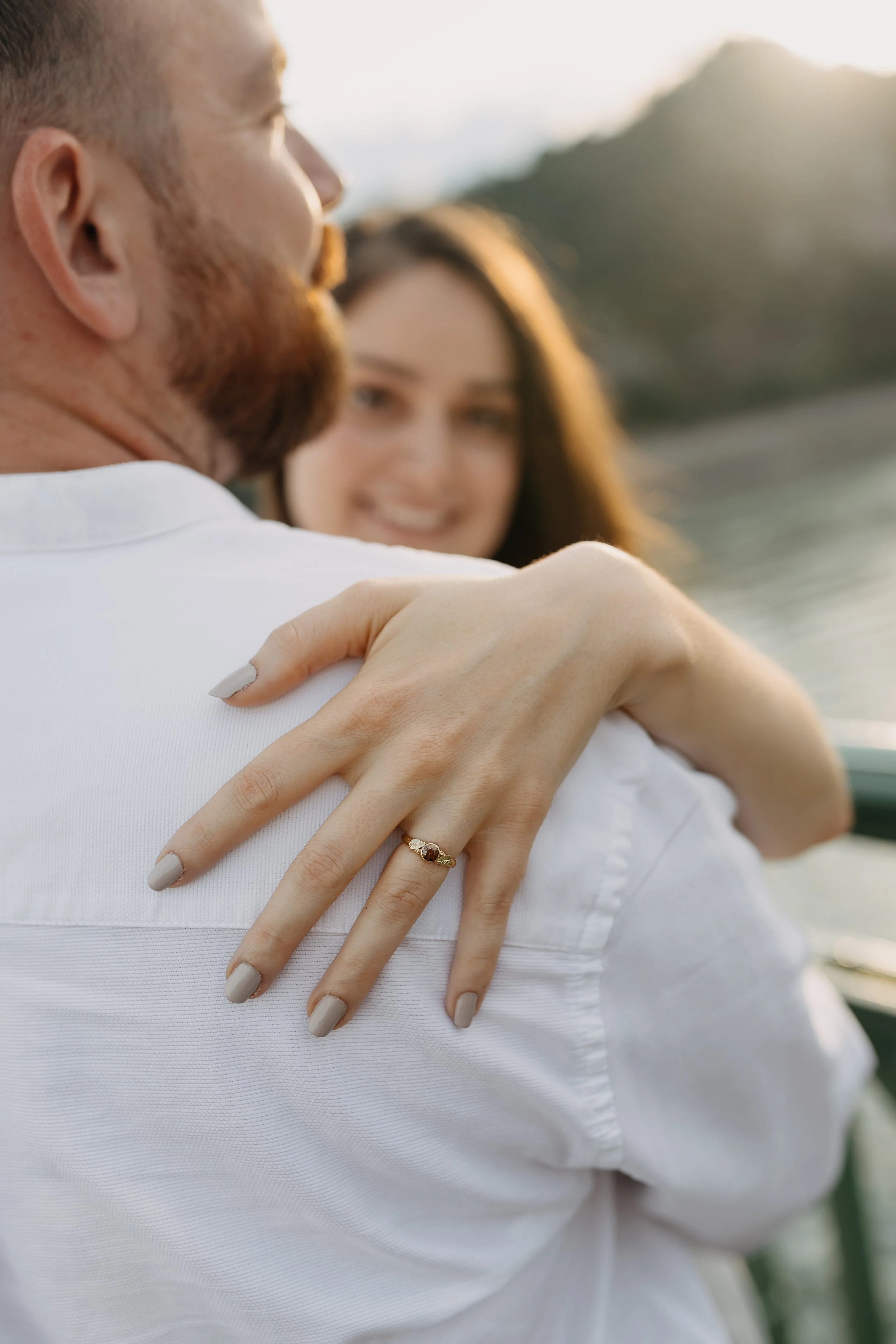 Close-up of a man with a beard and a woman smiling in the background, outdoor setting, warm sunlight.