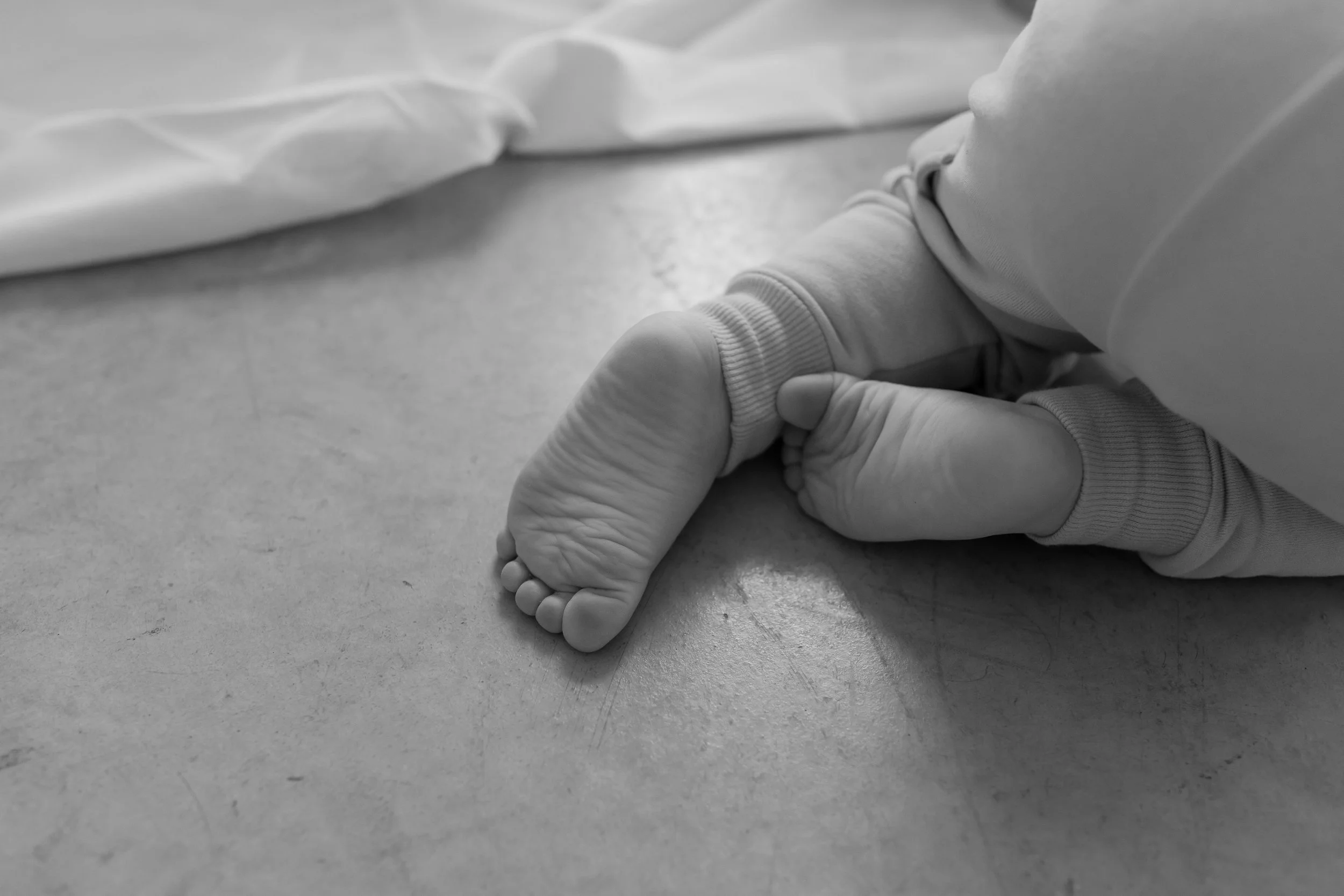 A pair of adult and baby hands holding each other on a smooth surface, with the baby’s tiny fingers wrapped around the adult’s finger.