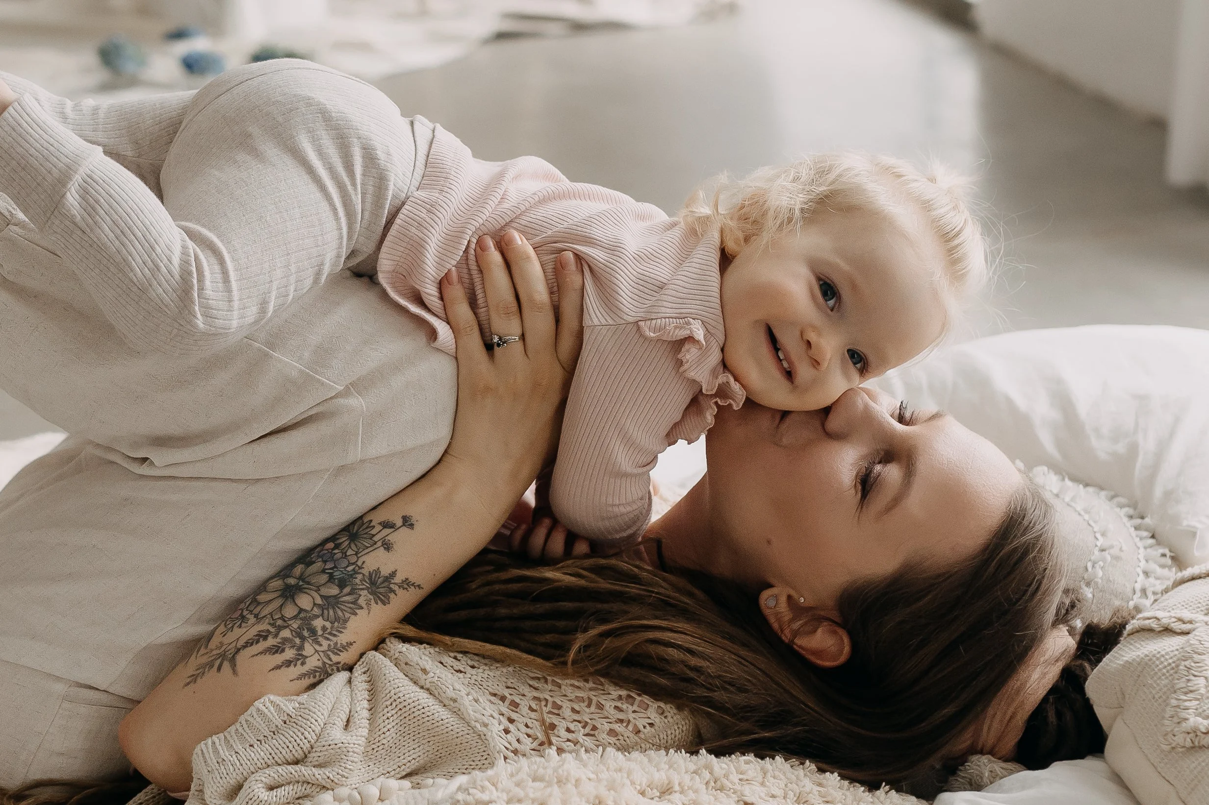 A woman lying on a bed and holding a smiling young girl, both relaxing and enjoying each other's company.