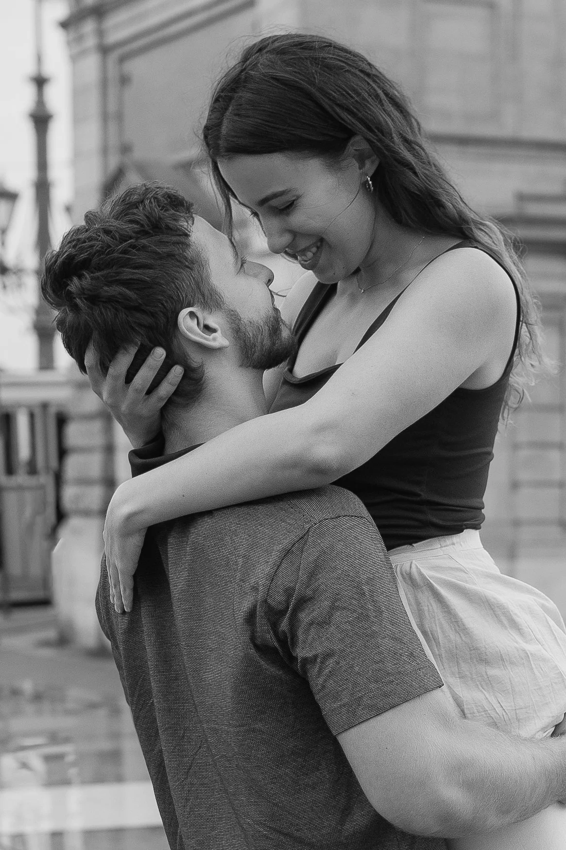 A couple shares a romantic moment outside, with the man lifting the woman. They are smiling and looking at each other affectionately.