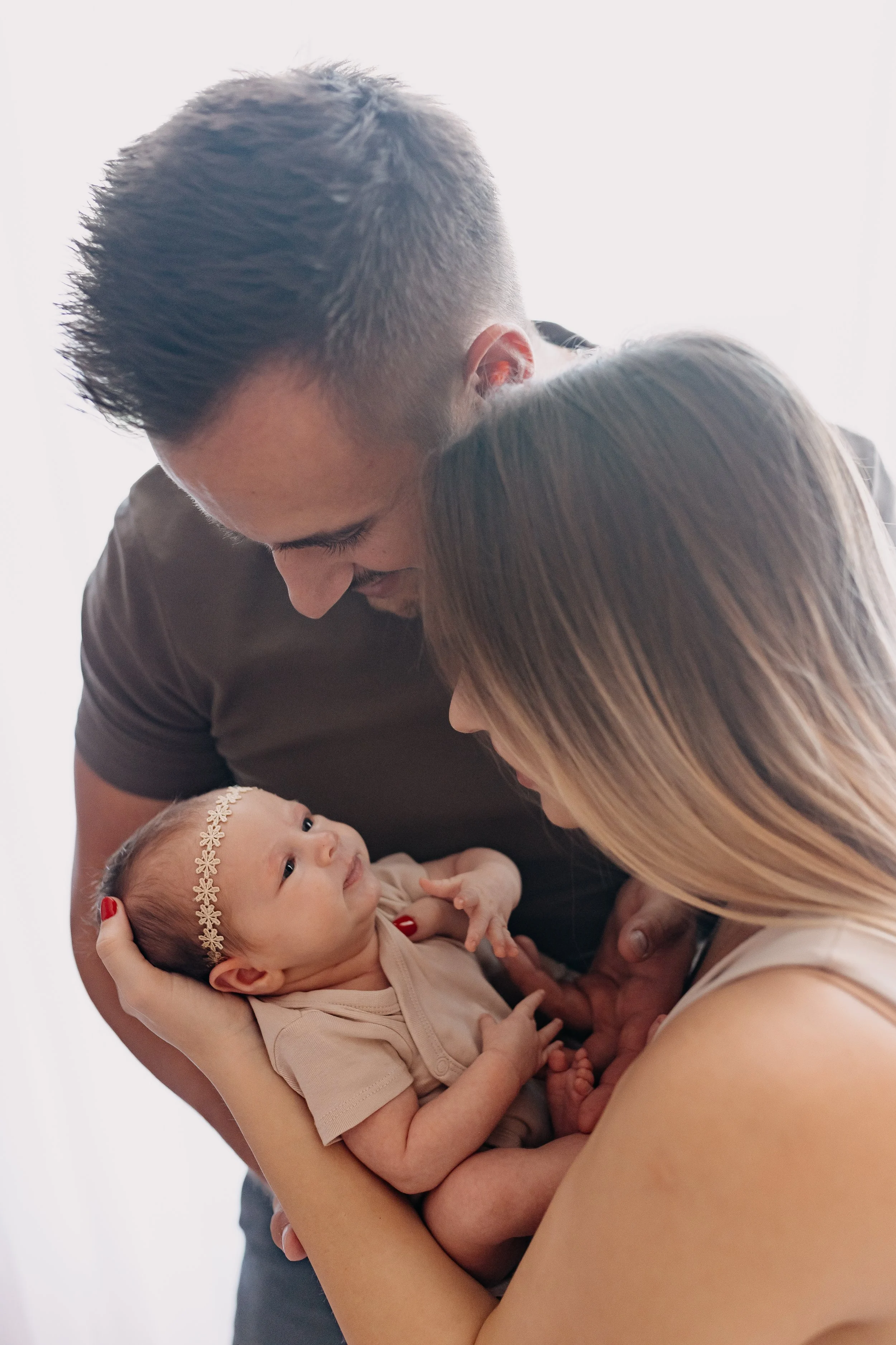 A family moment with a man, woman, and infant girl, all gazing lovingly at each other with the baby being held gently in the woman's arms.
