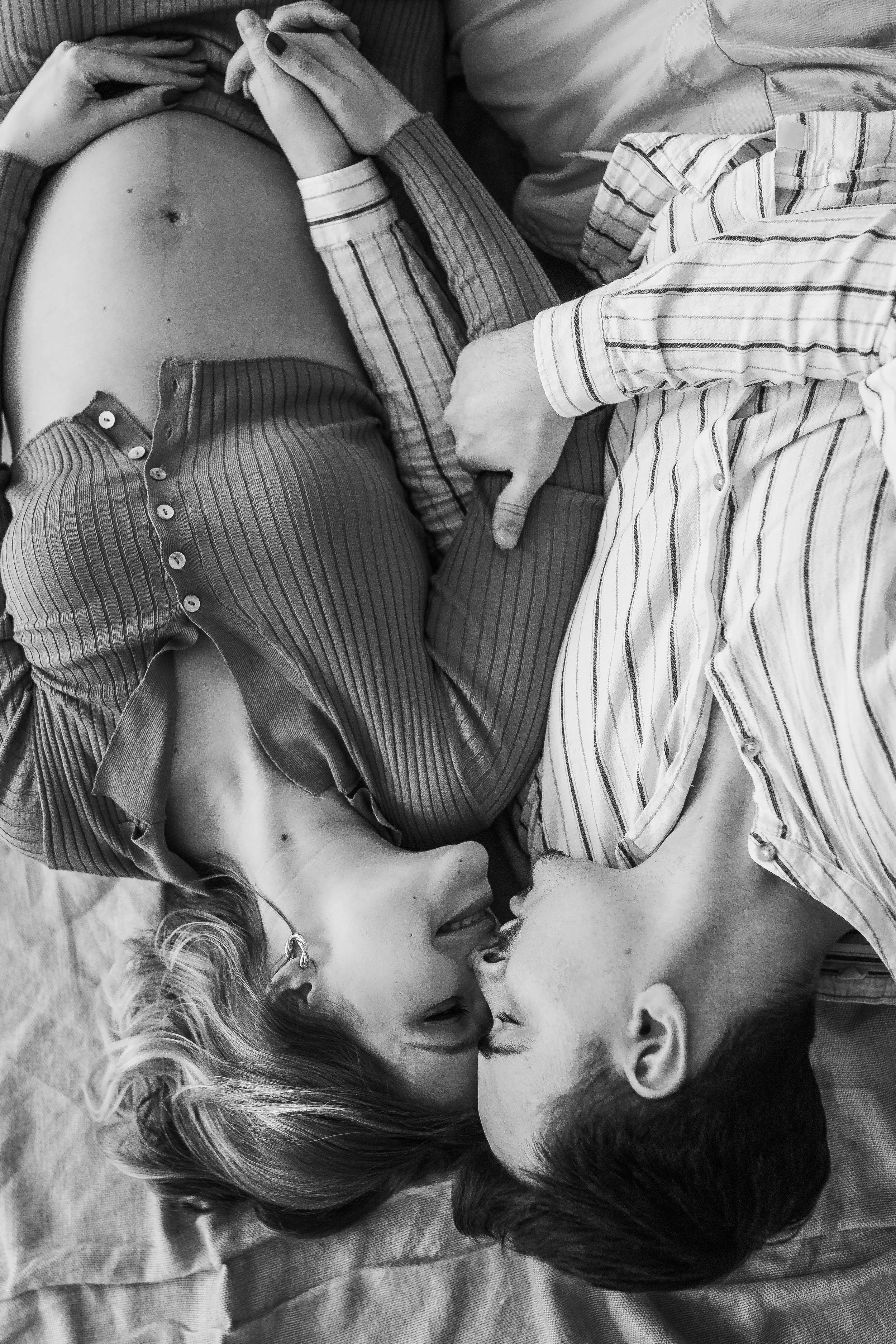 A black and white photo of a couple lying on their sides, facing each other, with their heads close together and their noses touching.