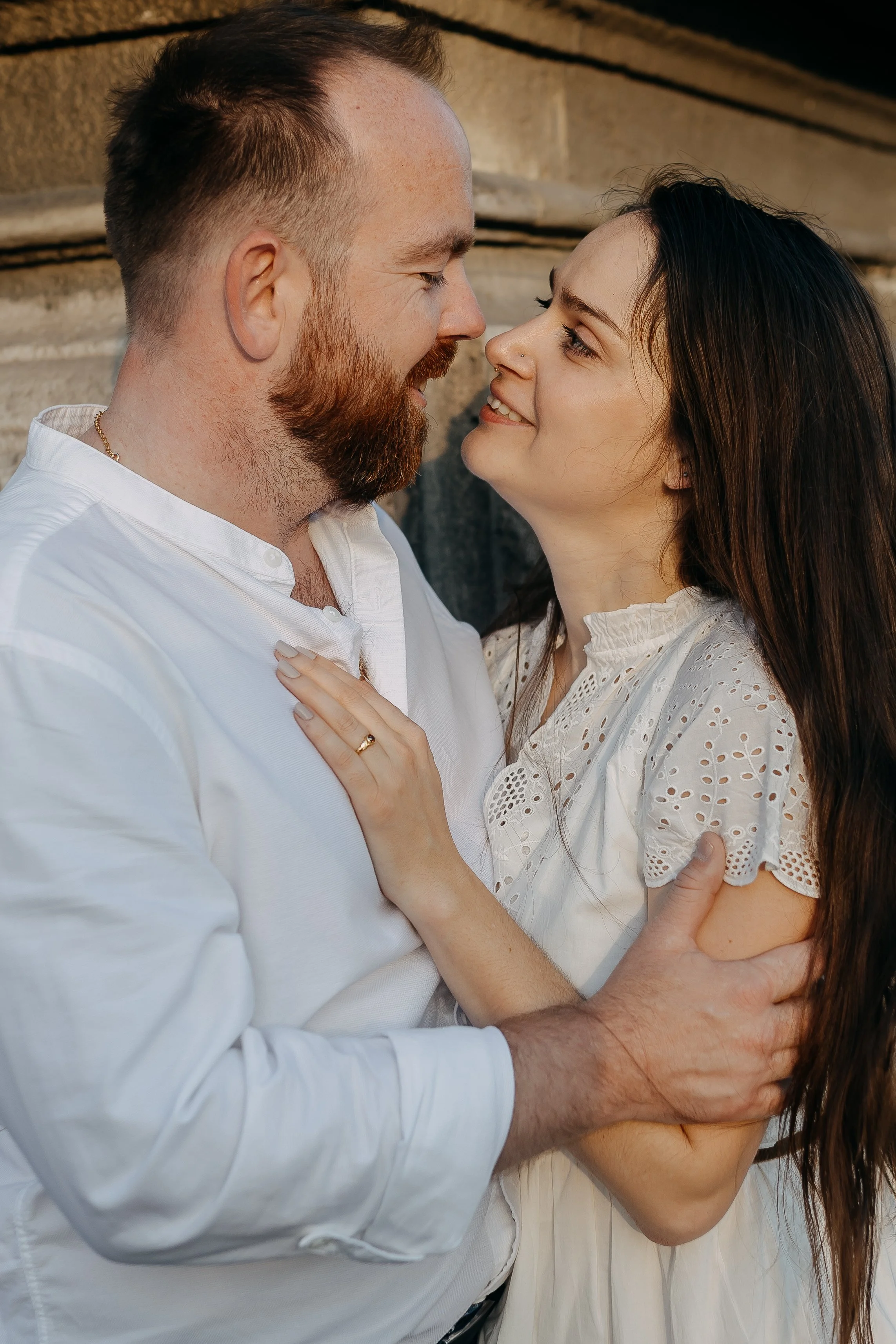 A couple with their foreheads and noses touching, smiling at each other, surrounded by a blurred background.