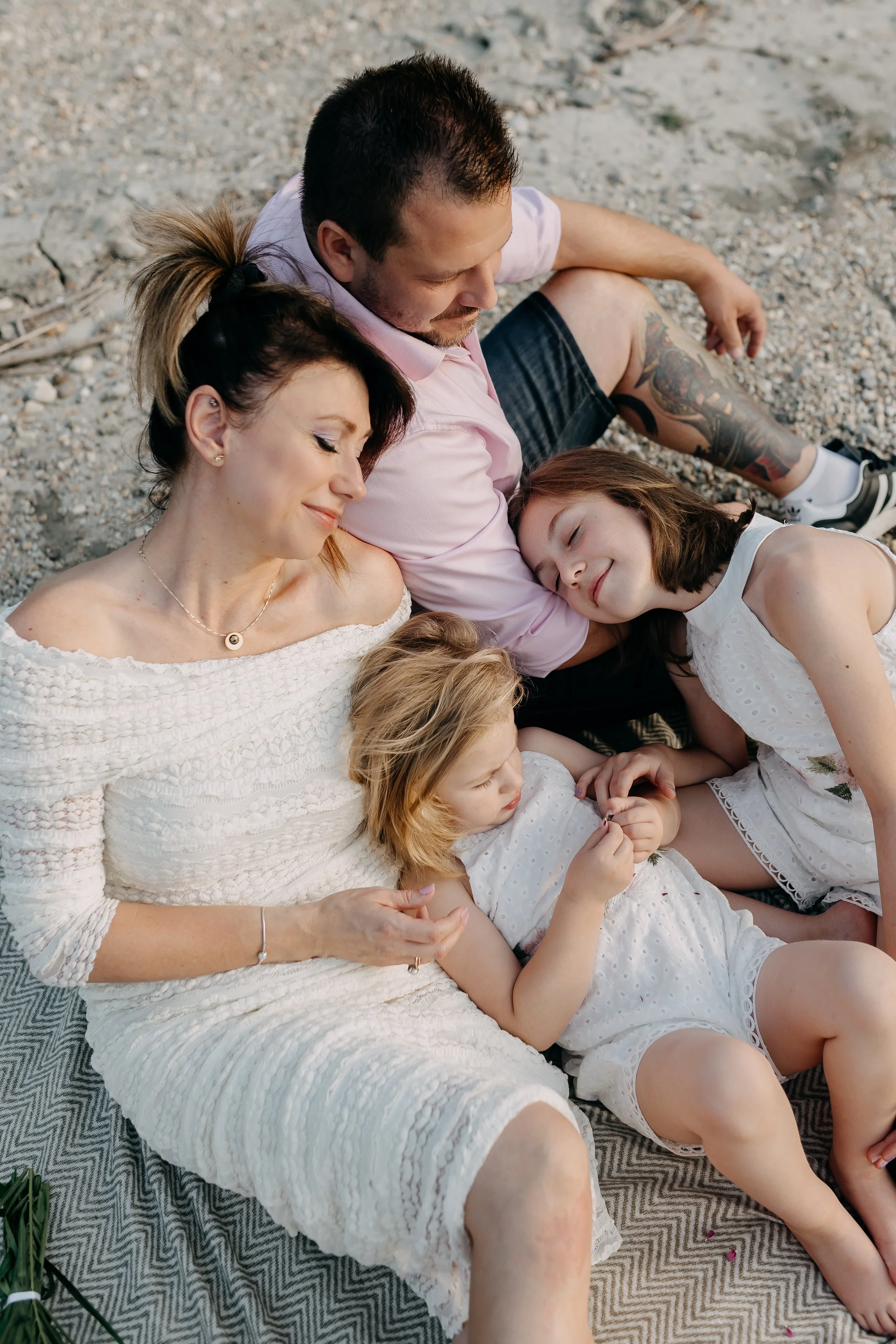 A family of five sitting on a patterned blanket on the ground, relaxing with eyes closed and smiling.