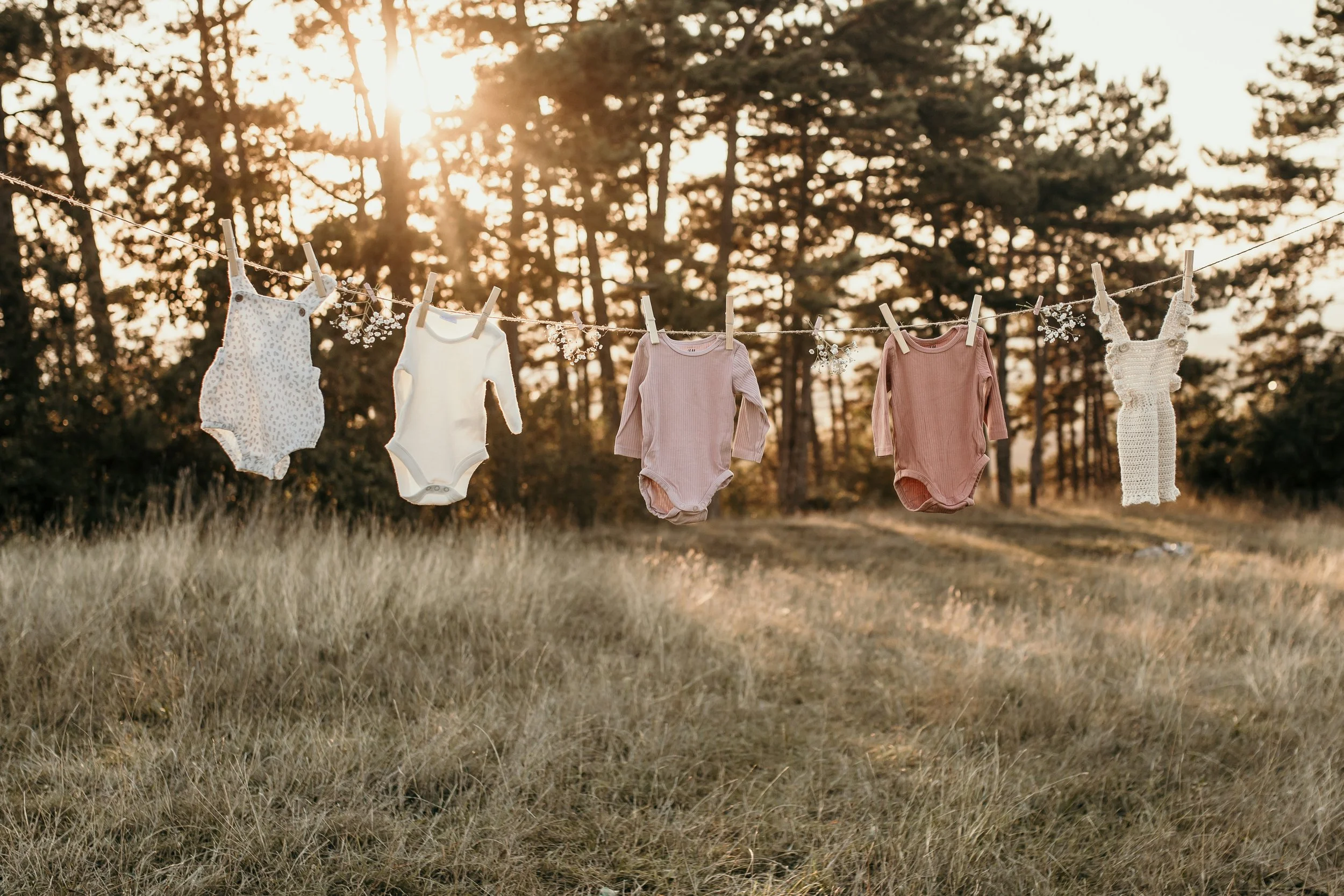 Baby clothes hanging on a clothesline outdoors during sunset, with trees in the background.