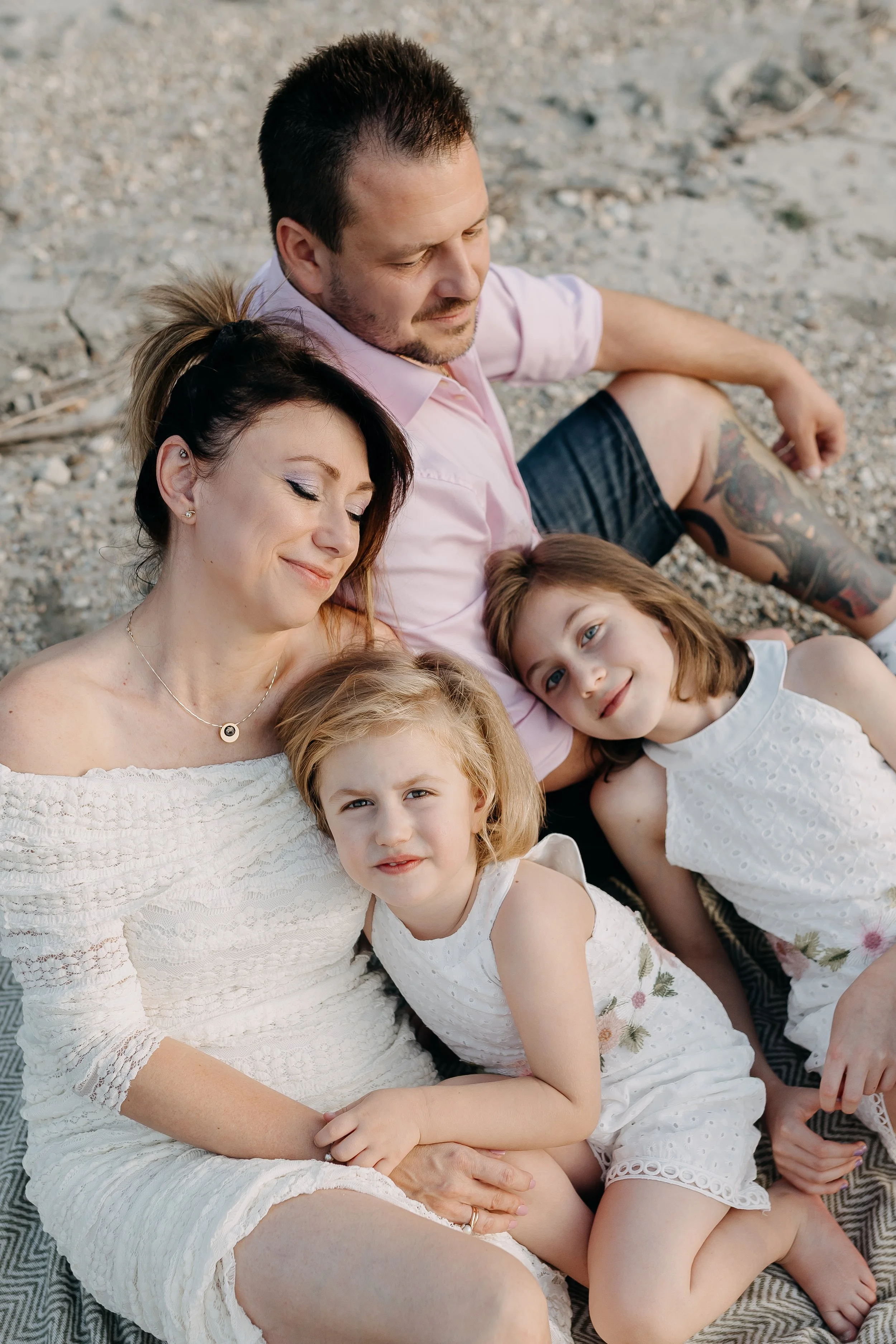 A family of five relaxing on a rocky beach, all dressed in light clothing and lying close together.