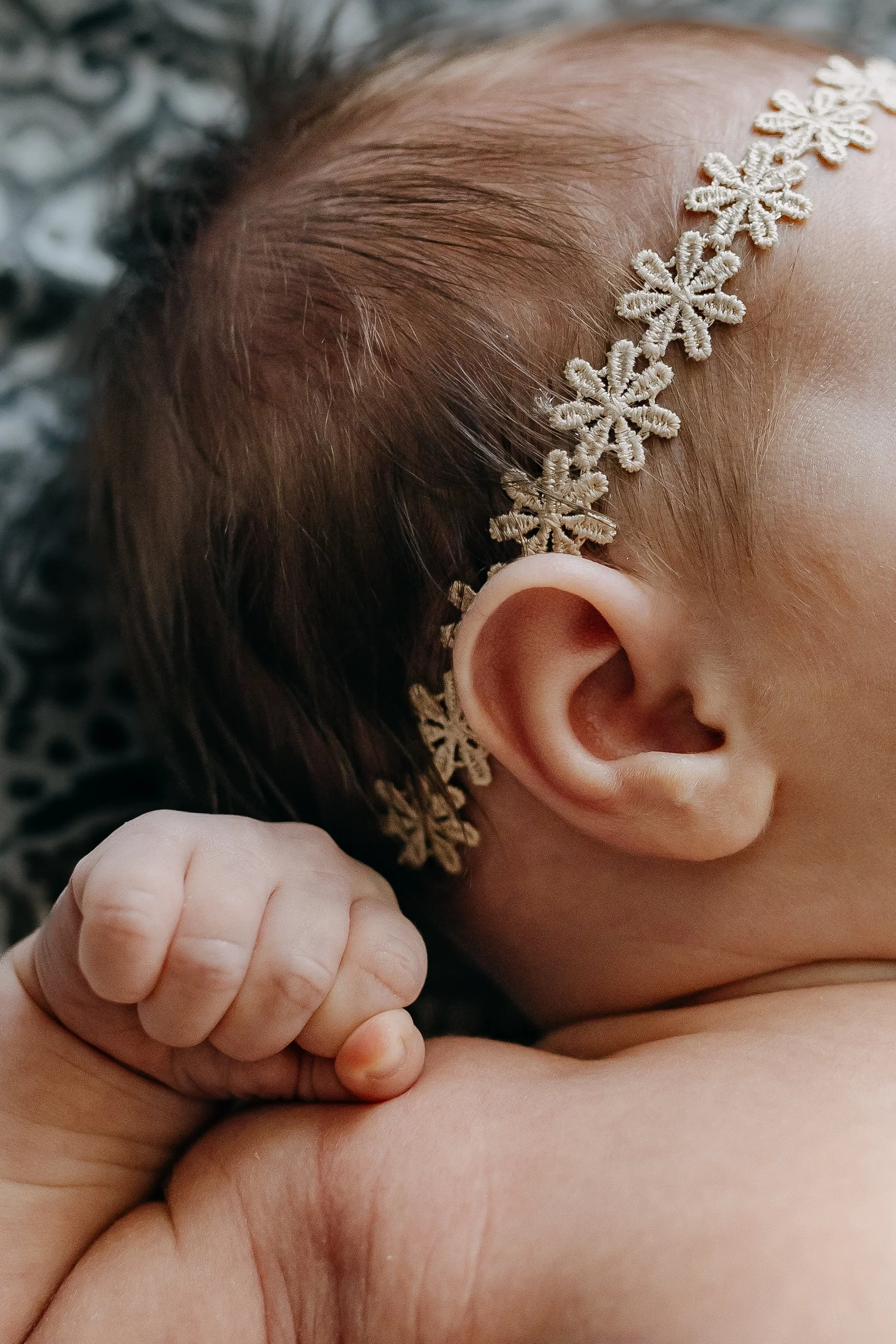 Close-up of a baby's head with a snowflake-shaped hair accessory and a hand gently touching their chest.