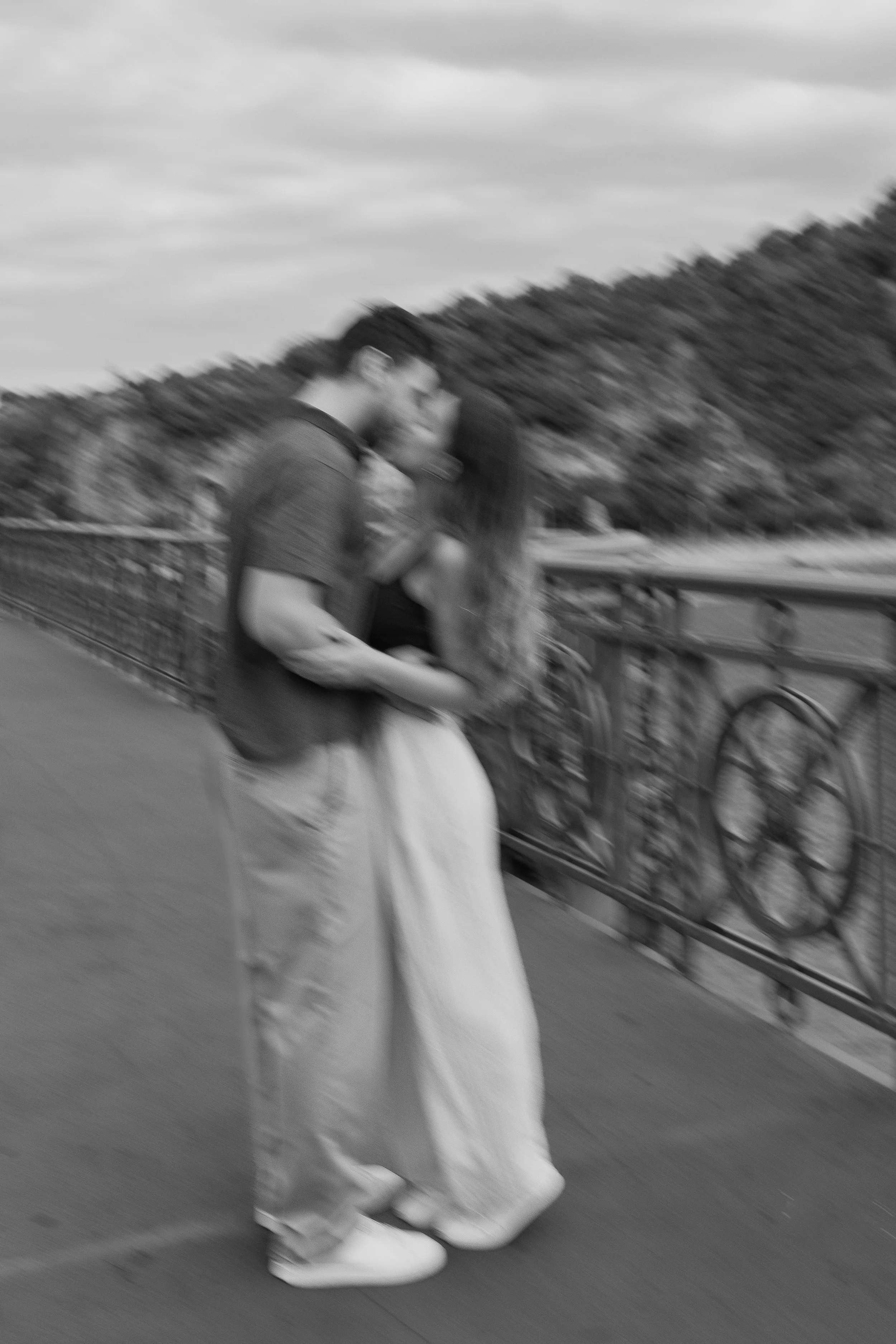Two people walking on a bridge, one in a long skirt and white shoes, the other in casual clothing. The photo is blurry and in black and white.