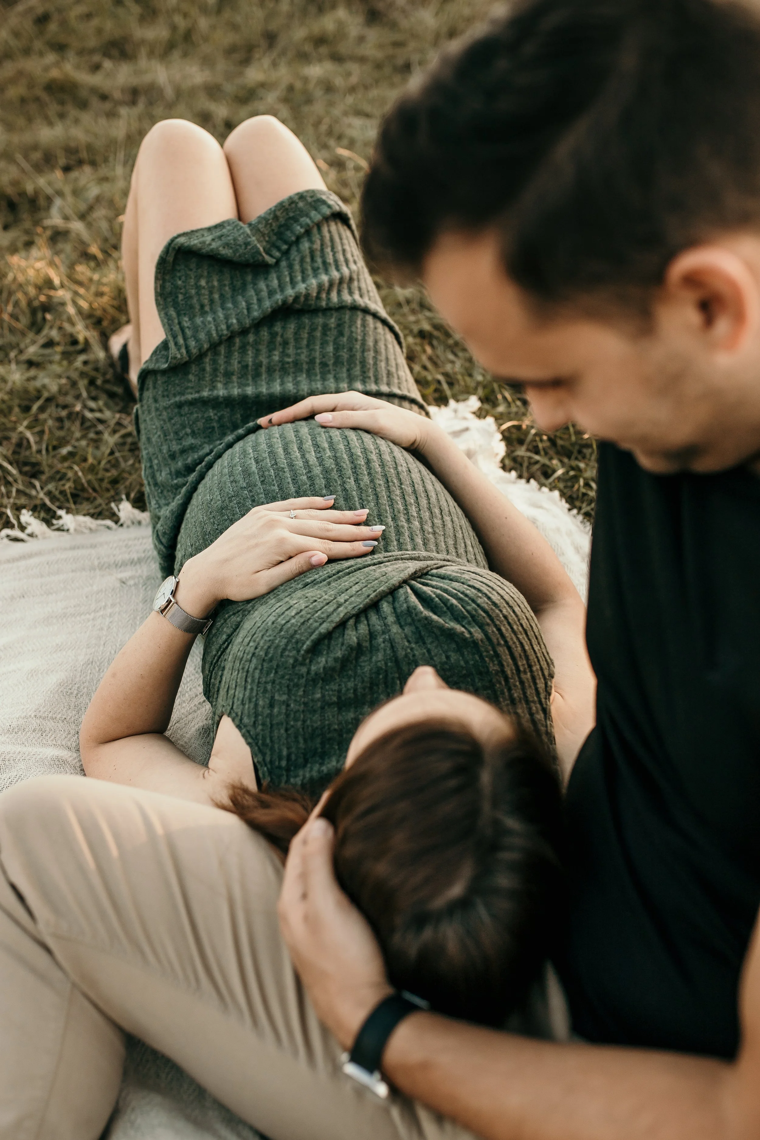 People lying on the ground outdoors, one person giving a massage to another, surrounded by grass.