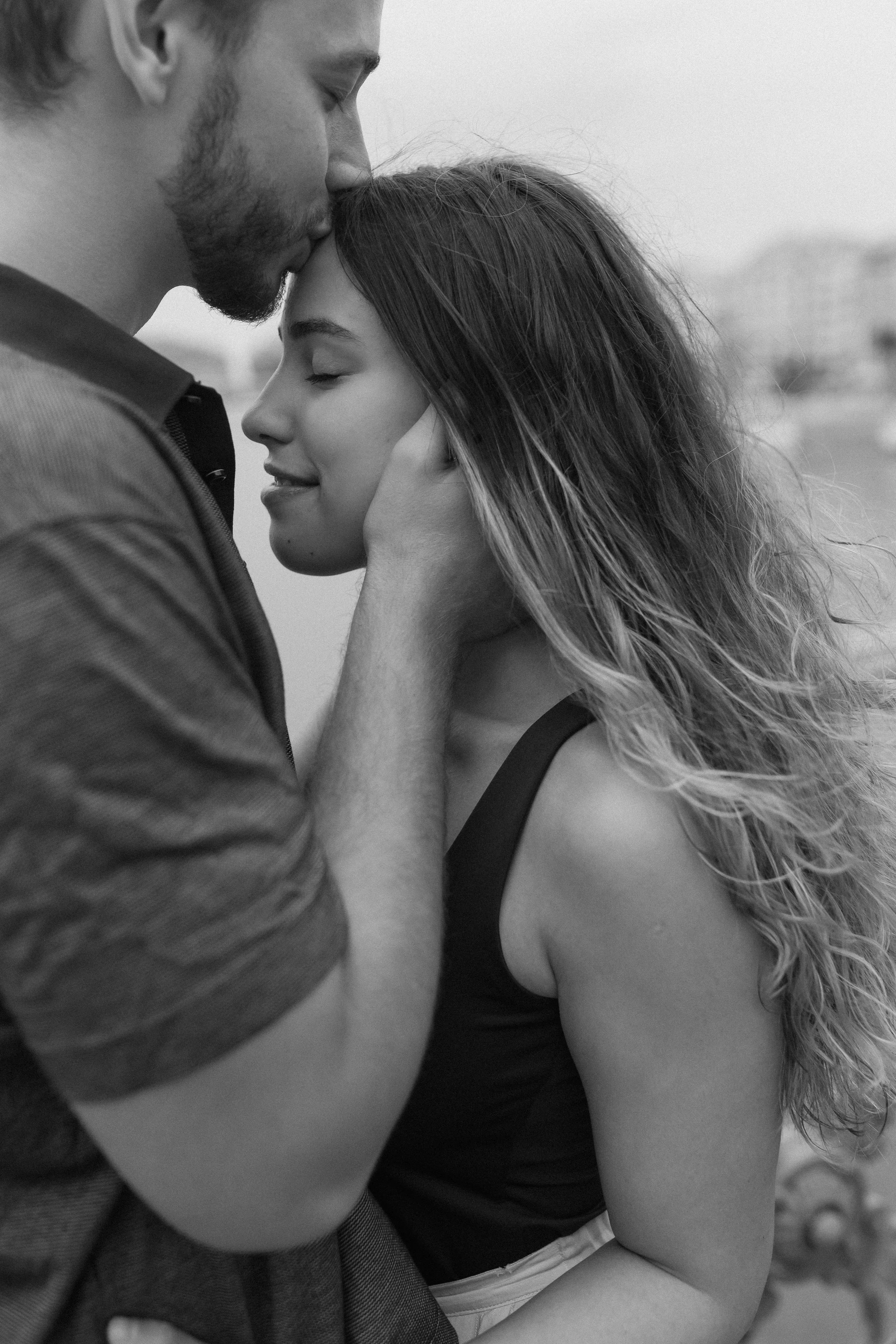 A black and white photo of a man and woman embracing closely. The man is kissing the woman's forehead, and she has her eyes closed, looking peaceful.