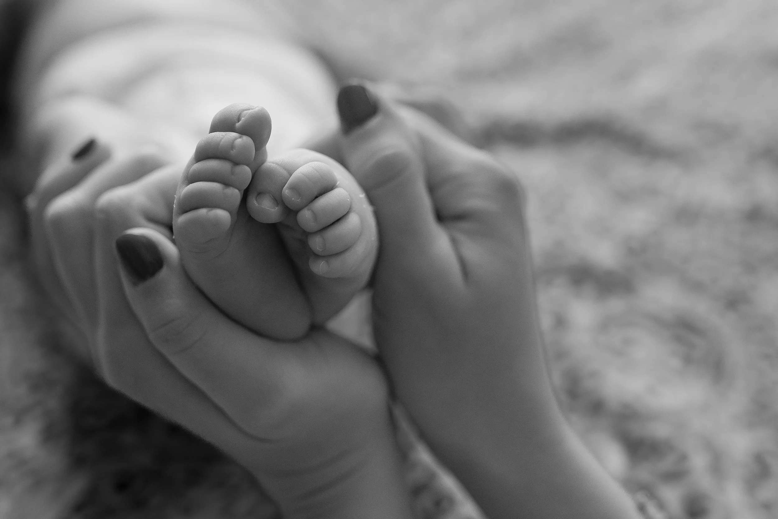 Black and white close-up of an adult holding a baby's hand in a gentle grasp.