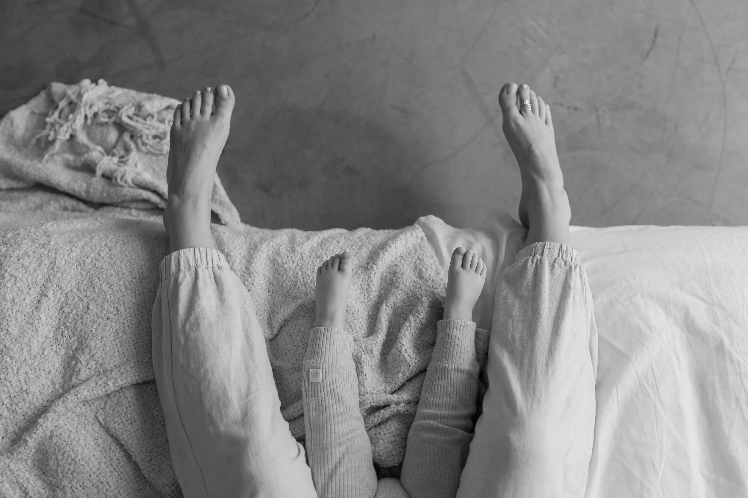 Black and white photo of a person's bare feet, with the toes and foot veins visible, resting on a textured surface, with a smaller child's bare feet nearby.