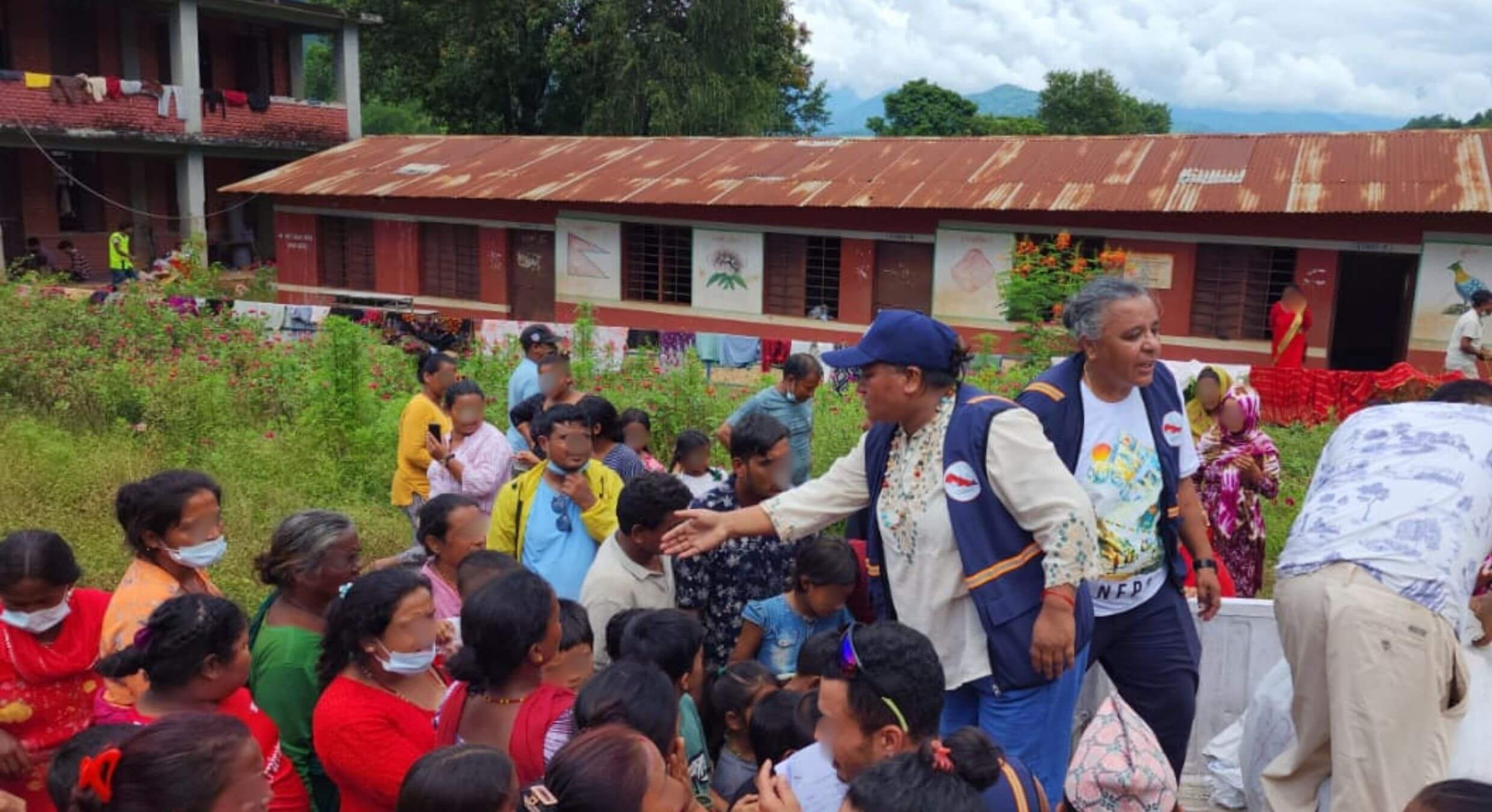 Teammitglieder von Change Action Nepal zwischen Frauen und Kindern auf einem Hof, daneben liegen Hilfspakete.