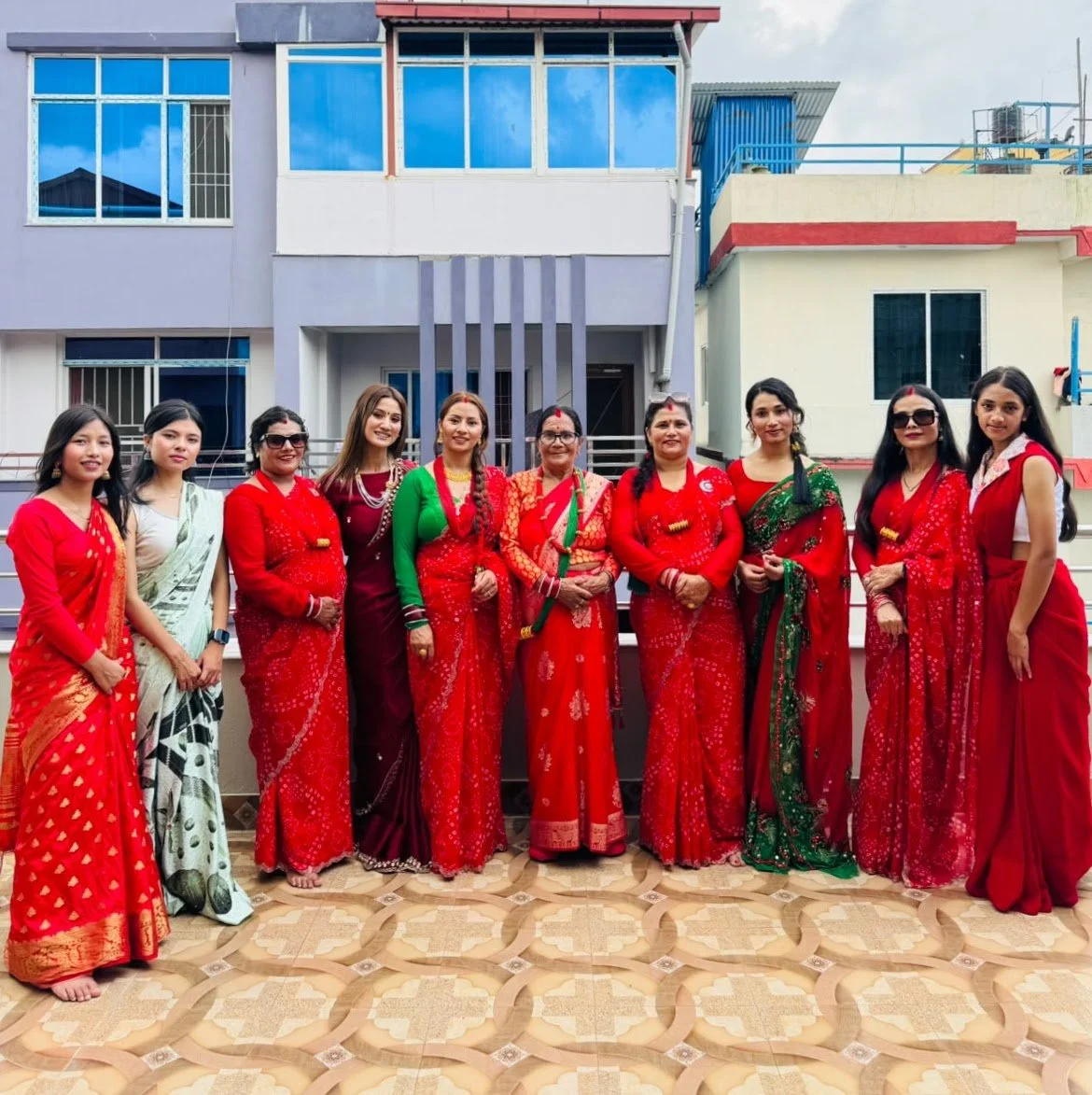 Frauen in roten und grünen Festkleidern stehen während einer Teej-Feier auf einer Terrasse in Nepal.