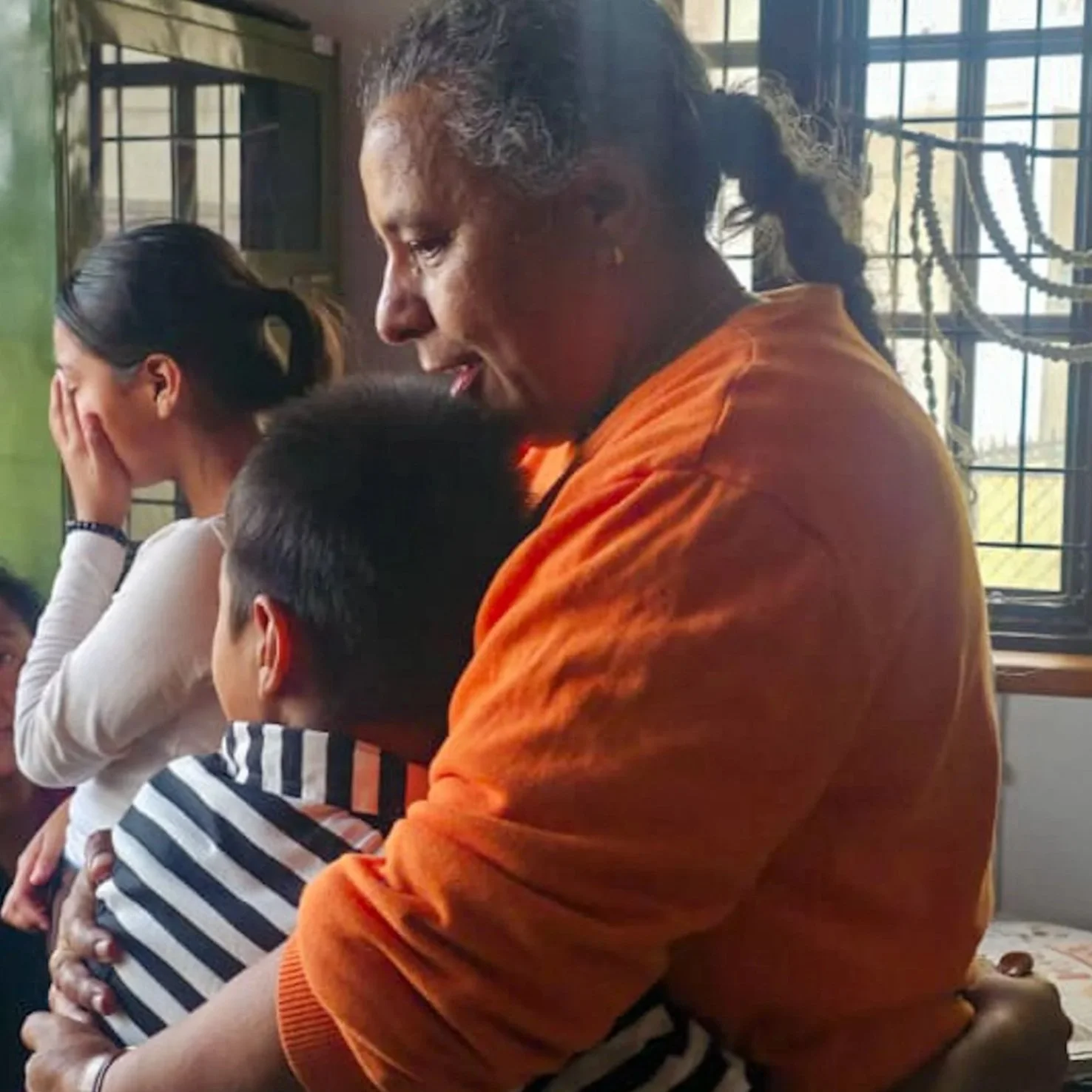 Indira Ghale von Change Action Nepal umarmt tröstend ein betroffenes Kind während eine weinende Frau im Hintergrund ihr Gesicht verdeckt.