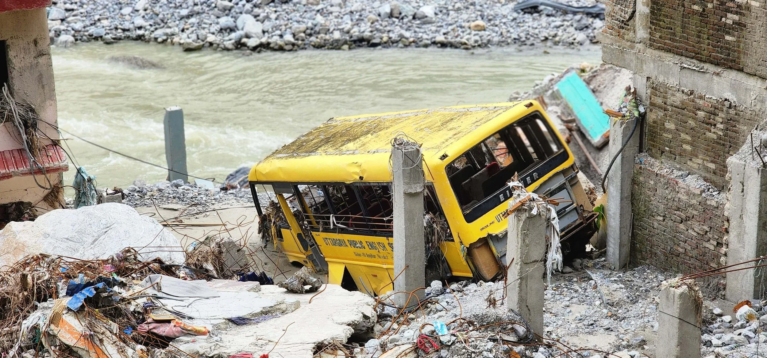 Gelber Bus zwischen eingestürzten Mauern und Betontrümmern an einem Fluss in Nepal nach der Sturzflut im August 2026.