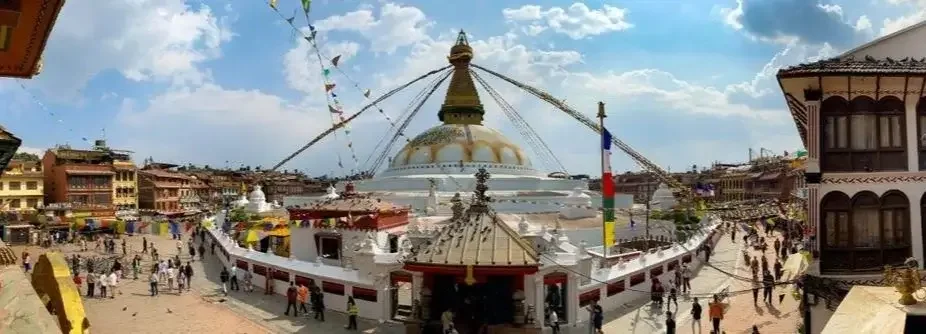 Panorama der weißen Kuppel der Boudhanath Stupa in Kathmandu, Nepal, mit den Augen Buddhas und bunten Gebetsfahnen unter blauem Himmel.