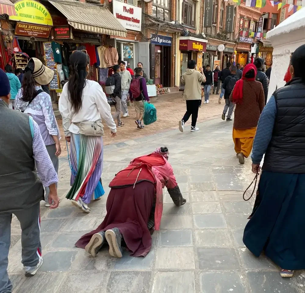 Pilgerin in roter Kleidung vollzieht eine rituelle Niederwerfung der Länge nach auf dem Steinboden des Pilgerwegs an der Boudha Stupa.