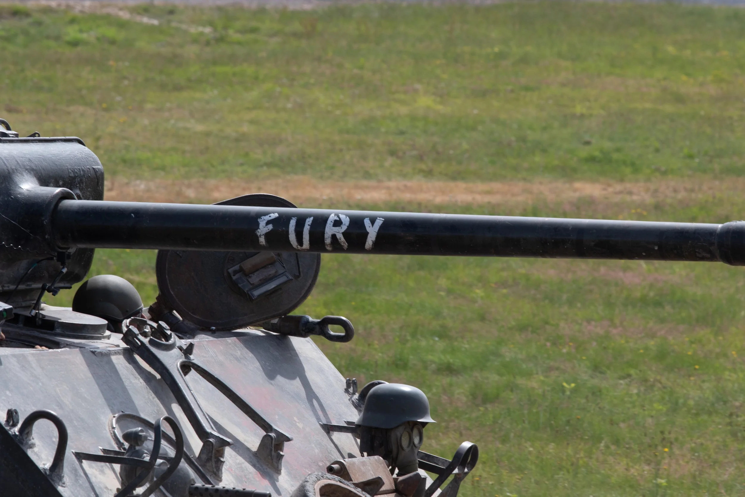 Close-up of a military tank with a gun barrel labeled 'FURY' in a grassy field.