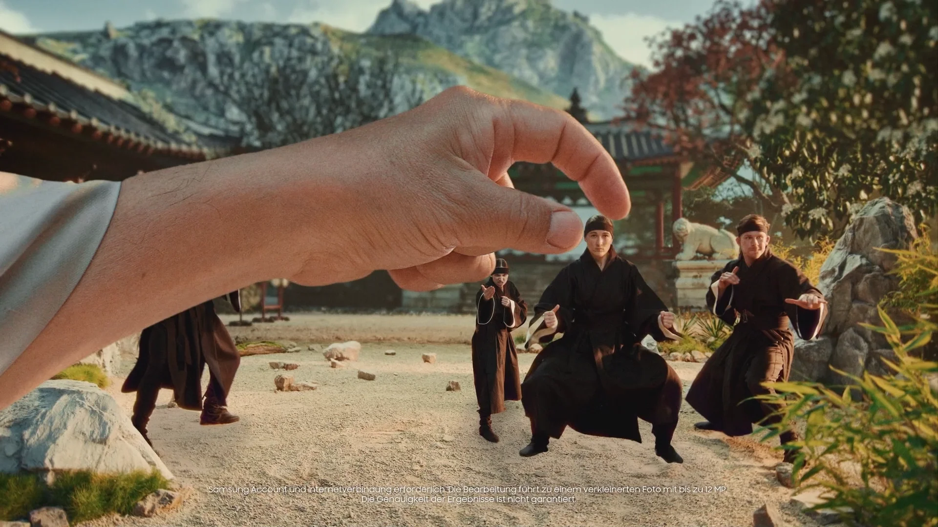 A large hand appears to be holding a scene with martial artists practicing in a traditional Asian courtyard, with mountains and pagoda-style buildings in the background.