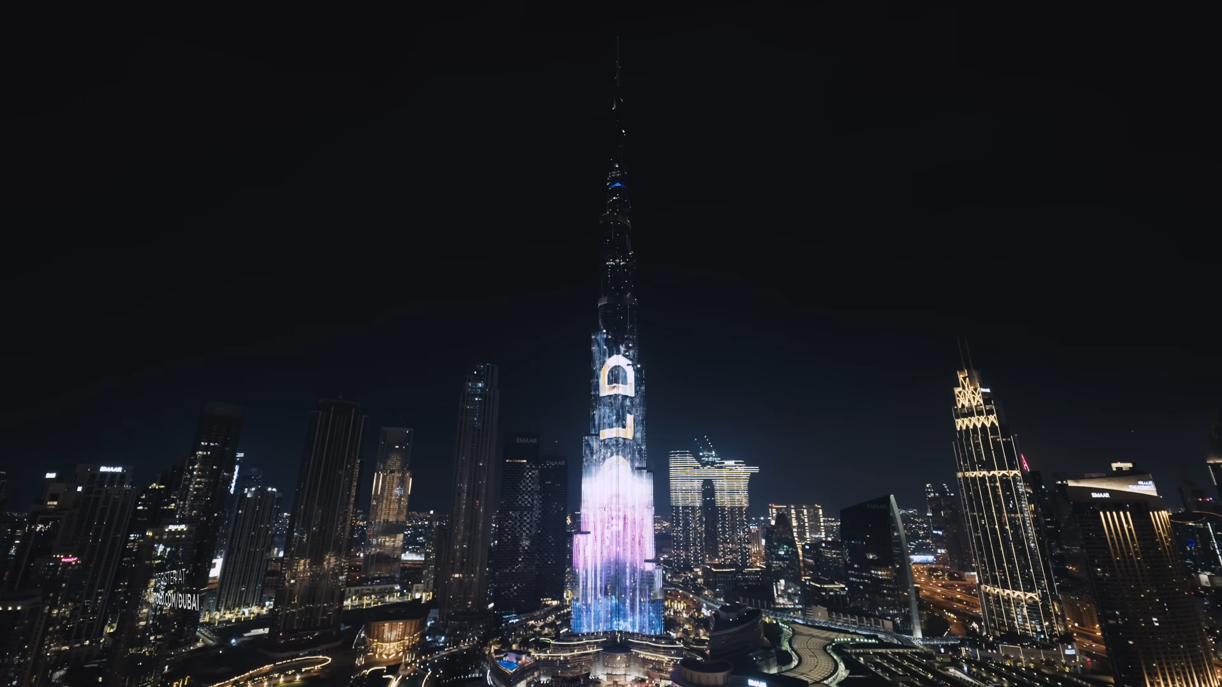 Nighttime view of Dubai skyline with illuminated Burj Khalifa, the world's tallest building, decorated with colorful lights and digital displays.