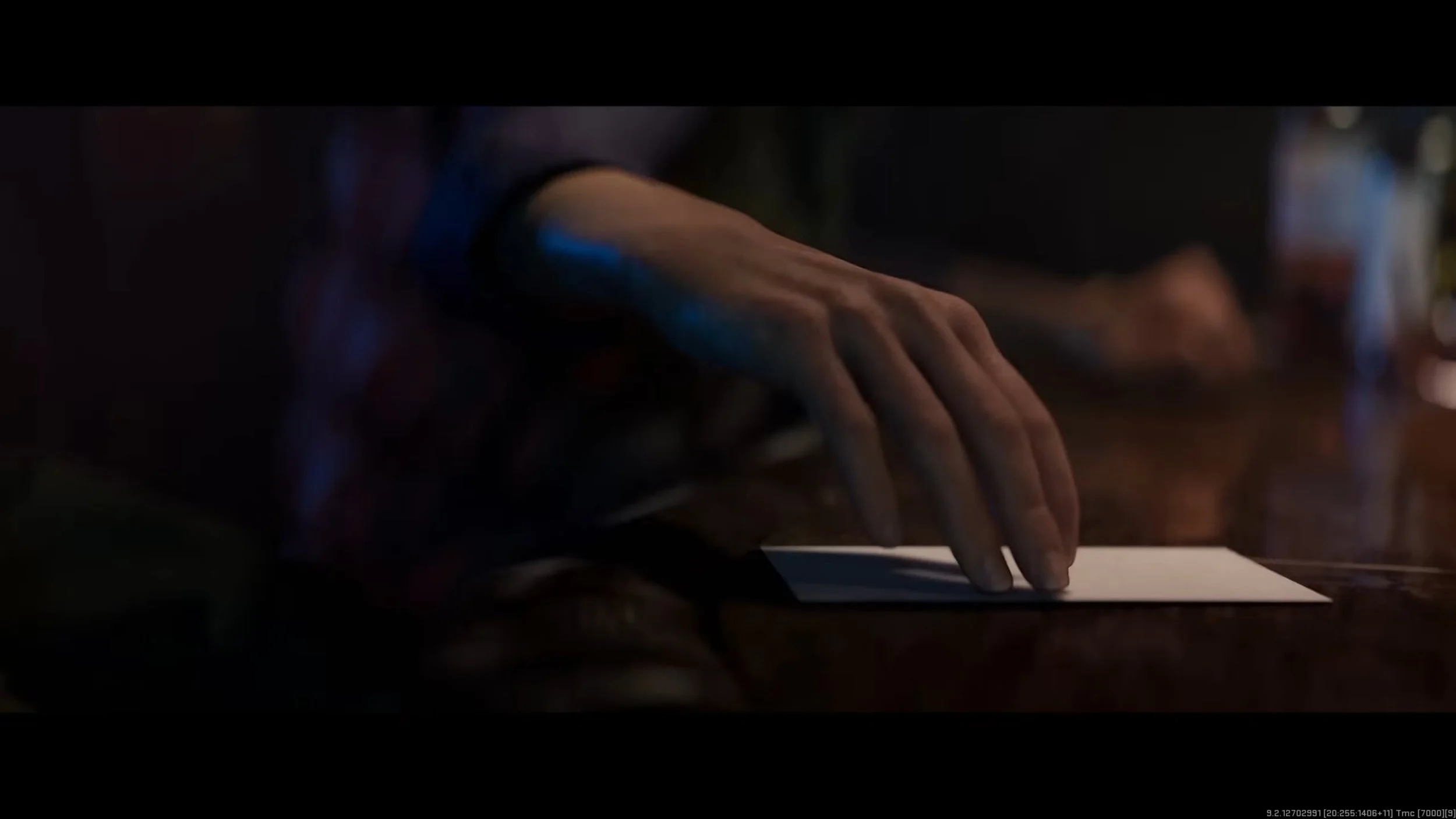 Close-up of a person’s hand resting on a table near a sheet of paper, with a dark background and soft lighting.