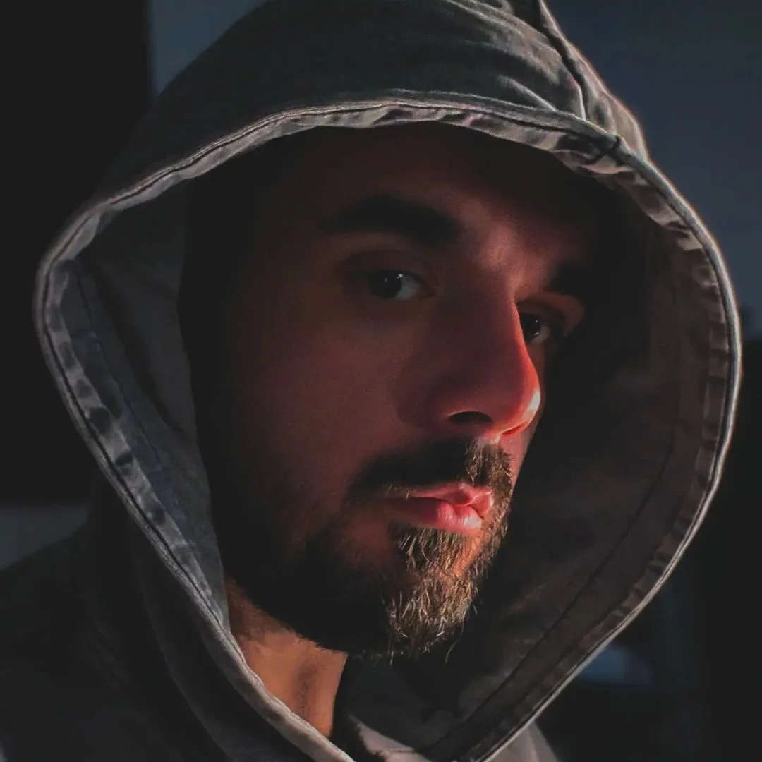 Close-up of a man wearing a hooded jacket, looking to the side in low light.