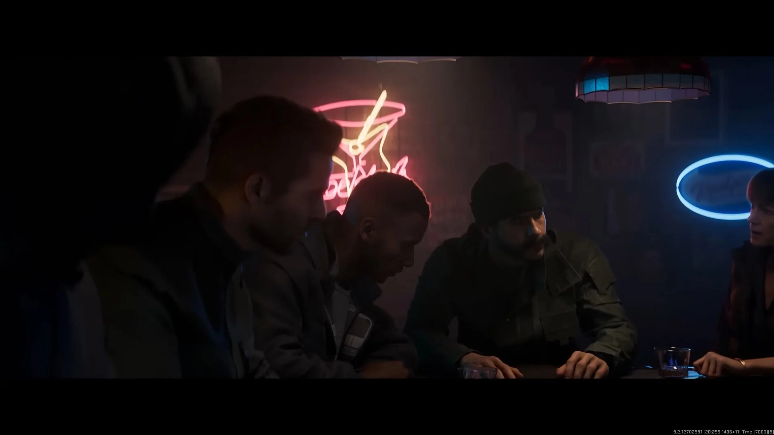 Four men sitting at a table in a dimly lit room with neon signs, including a pink coffee cup and a blue oval, behind them.