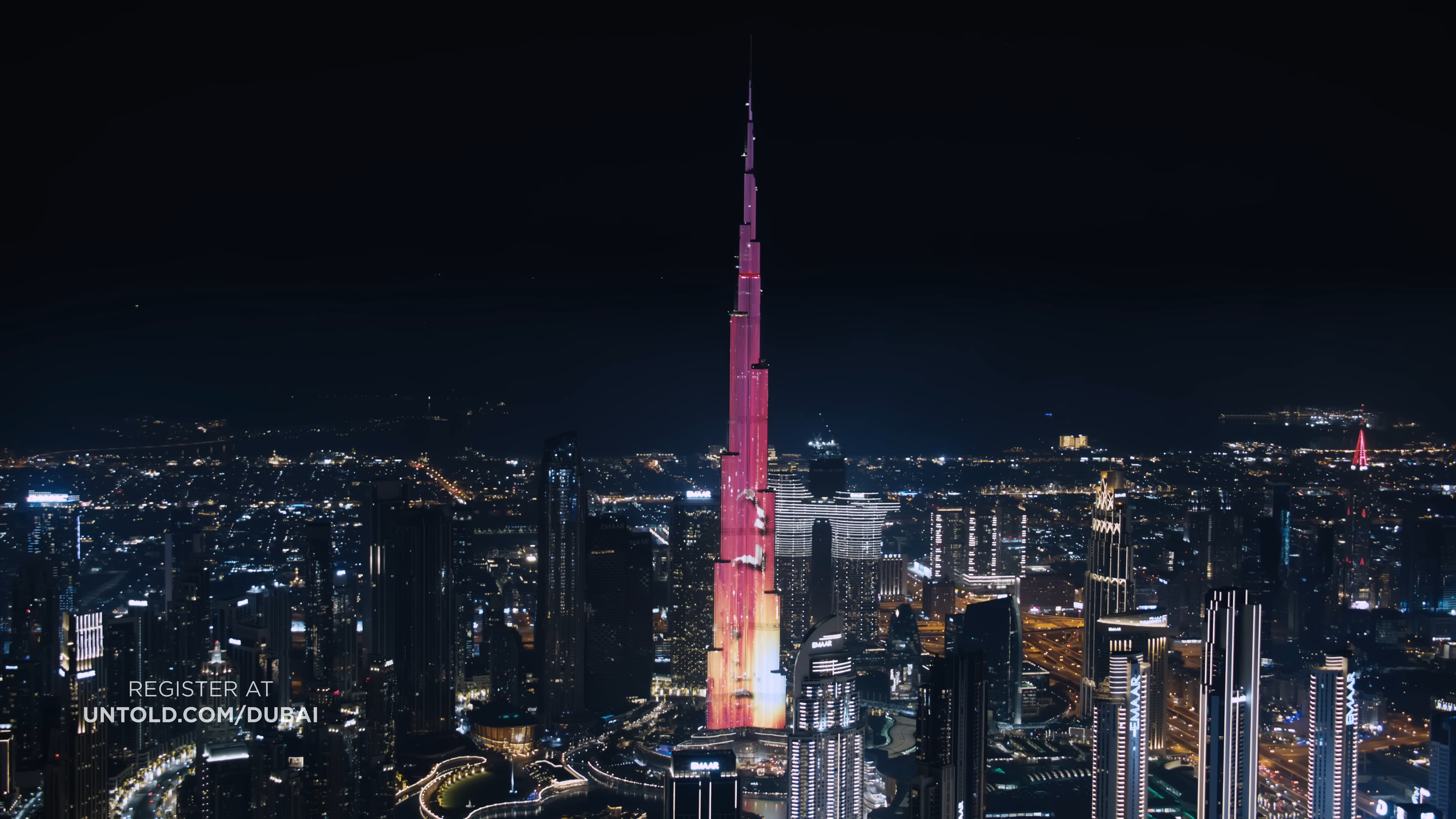 Night view of Dubai with illuminated skyline and the Burj Khalifa tower lit in pink and purple lights.