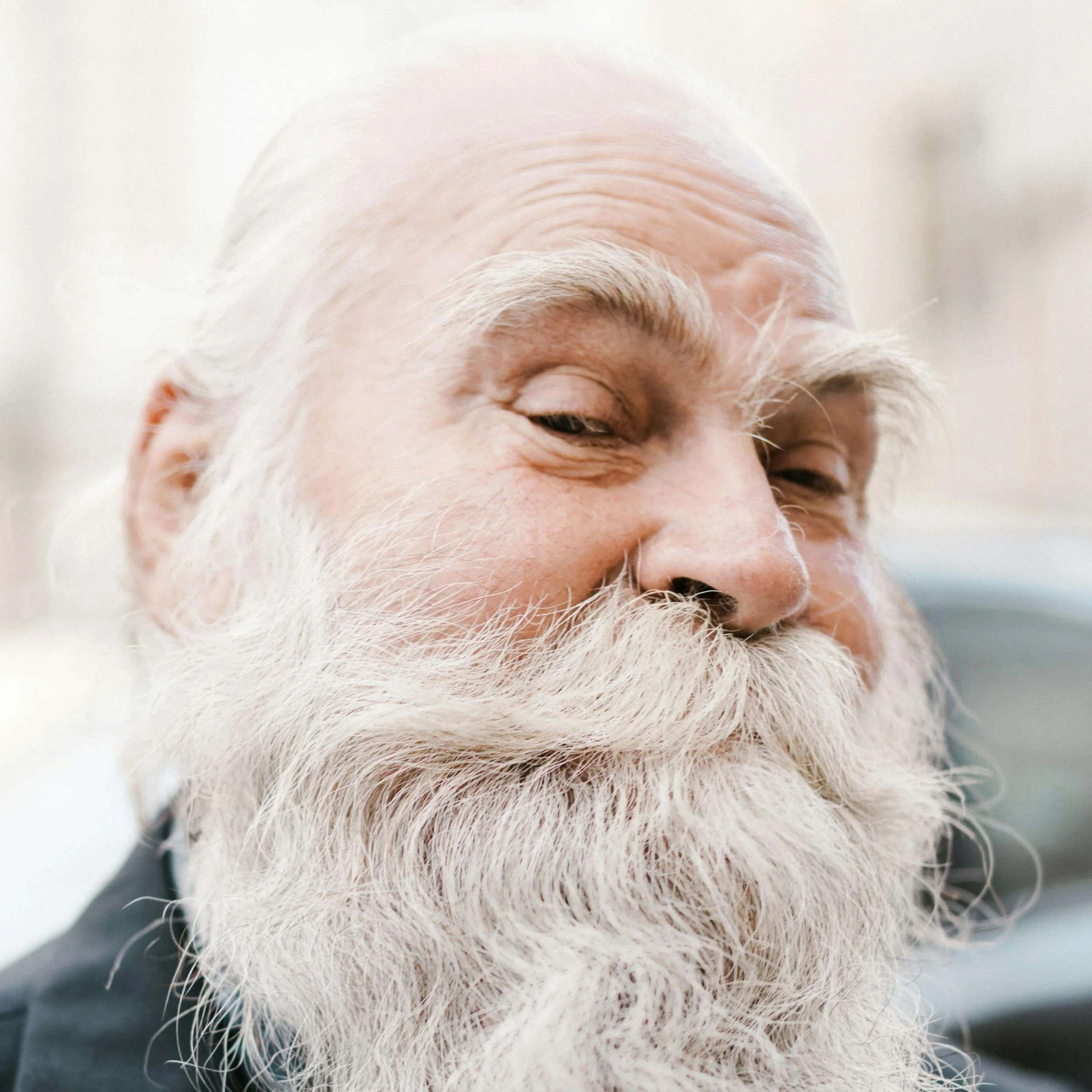 Close-up of an elderly man with white hair and a large white beard, smiling with his eyes partly closed.