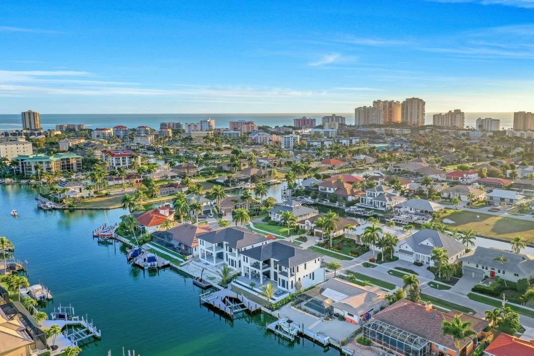 Aerial view of a coastal city with waterfront houses, canals, and high-rise buildings in the distance during daytime.