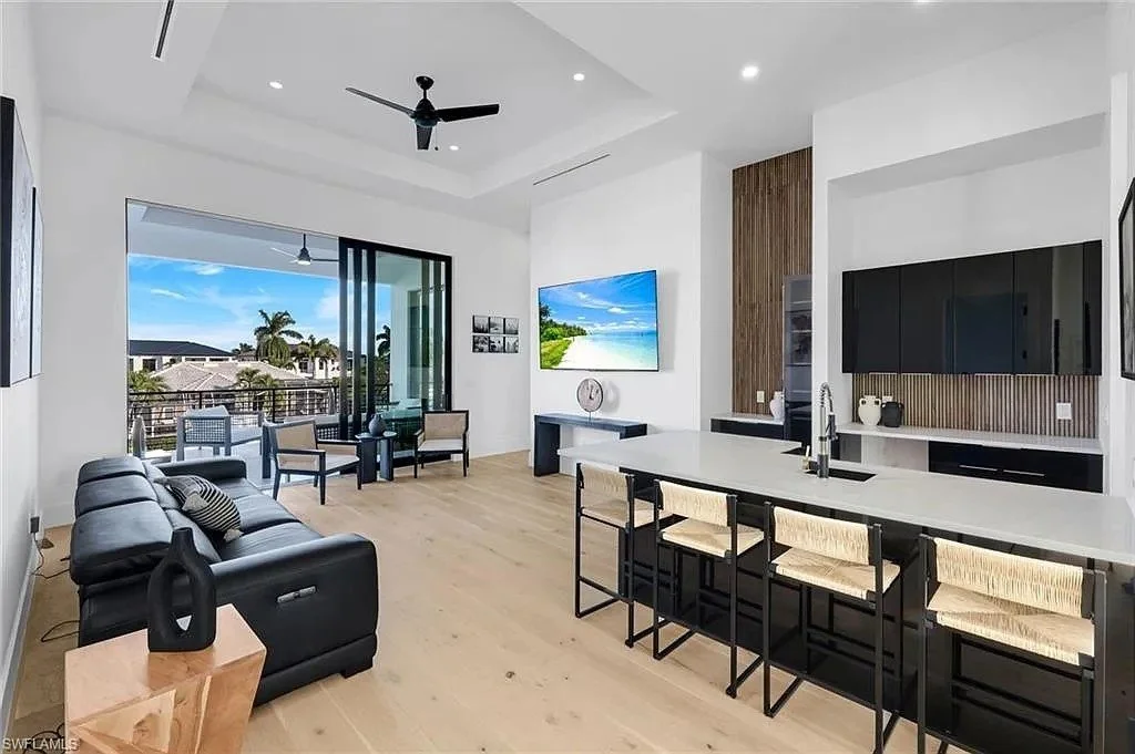 Open-concept living room and kitchen with large window and balcony, modern furniture, wall-mounted TV, and ceiling fan.