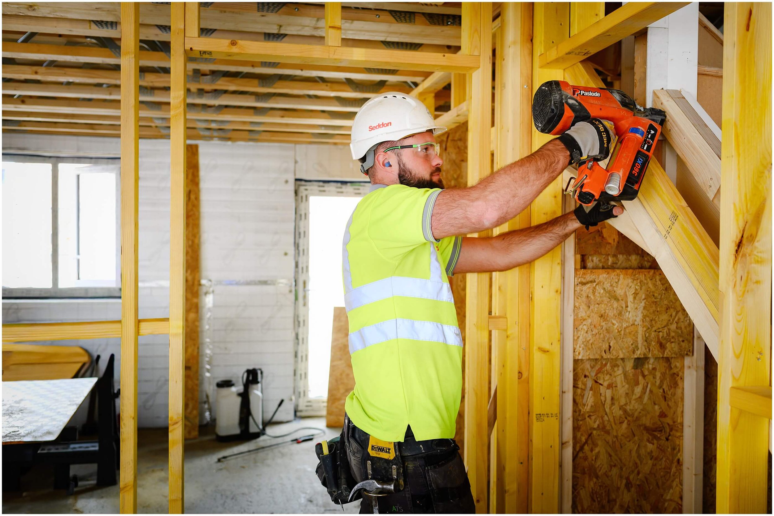 Construction worker in safety gear using a Paslode nail gun to frame an interior wall