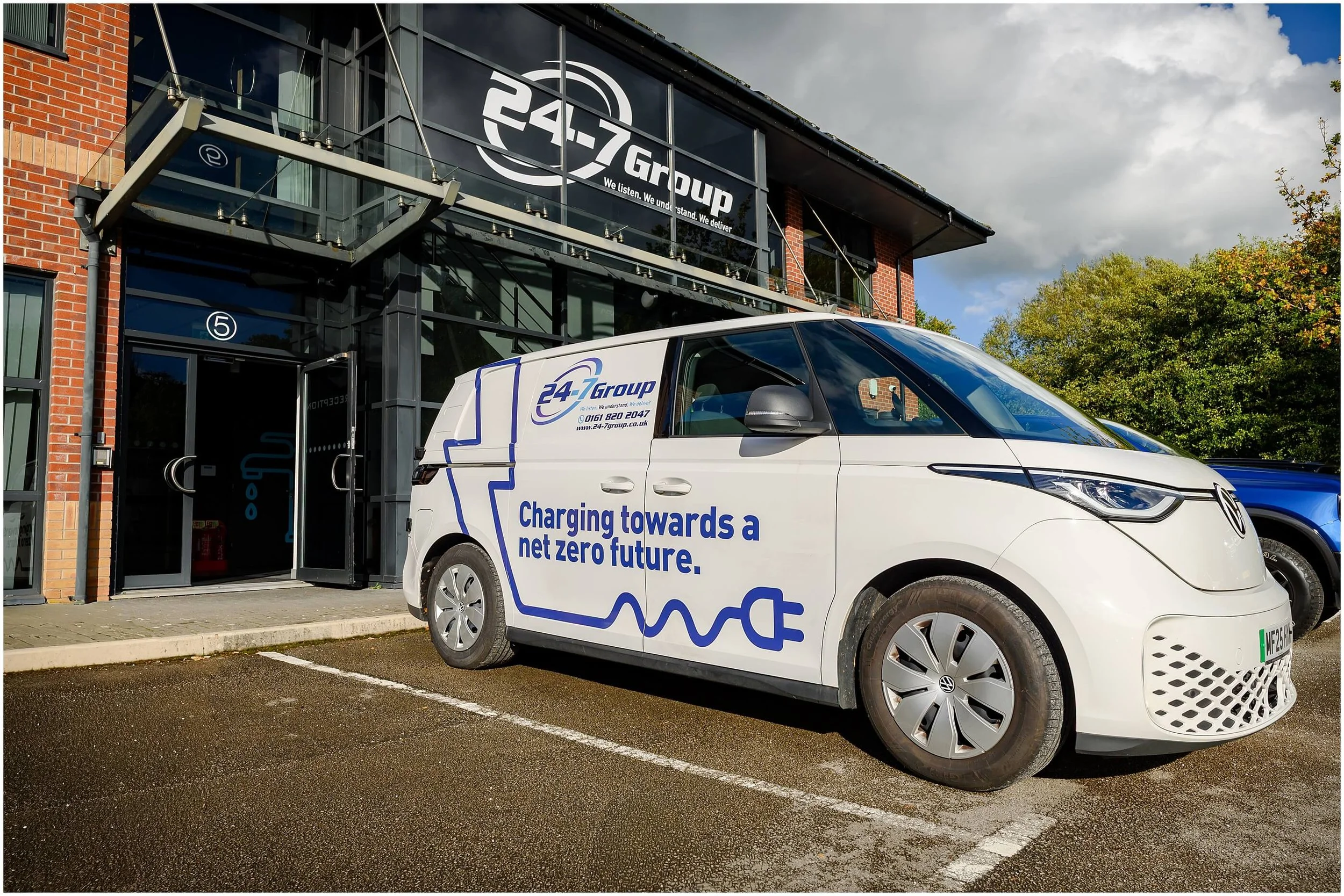 Branded electric Volkswagen van parked outside a 247 Group office building with brick walls and glass facade.