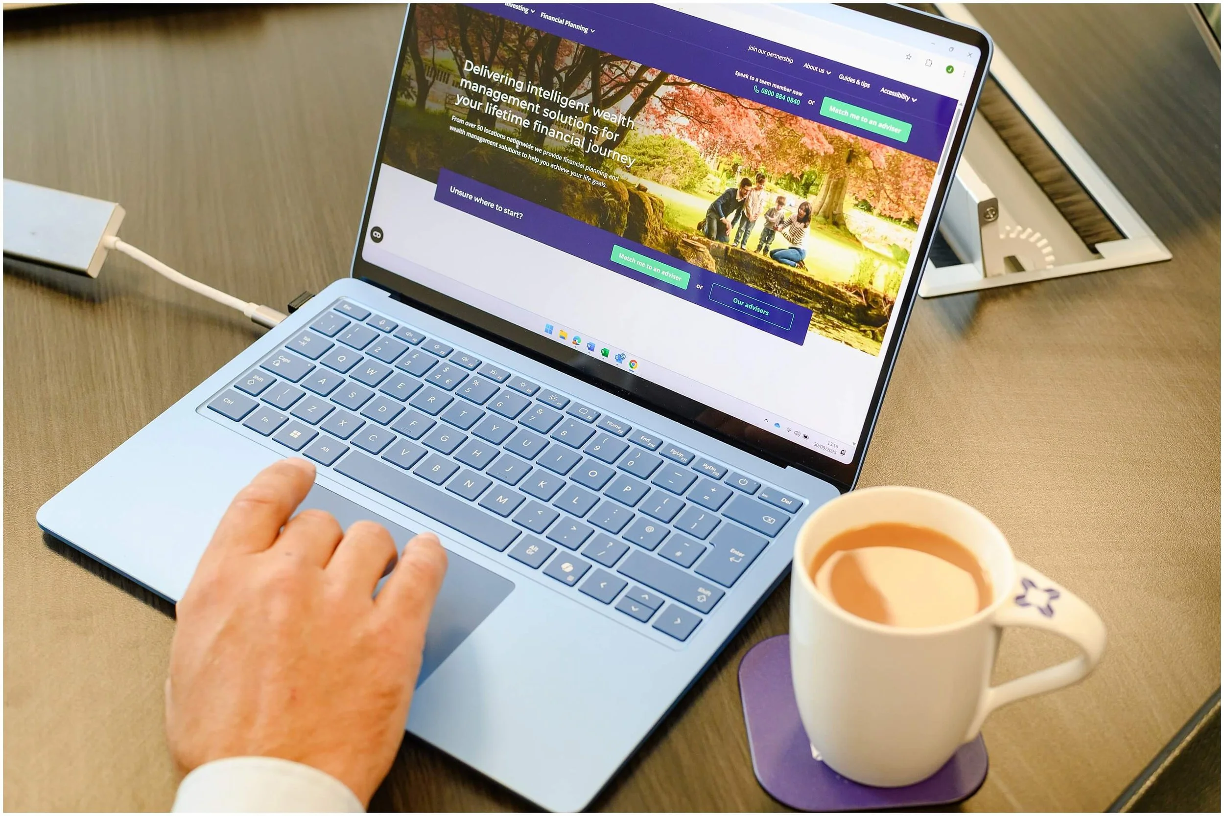 Person using a laptop to browse a wealth management website beside a cup of coffee