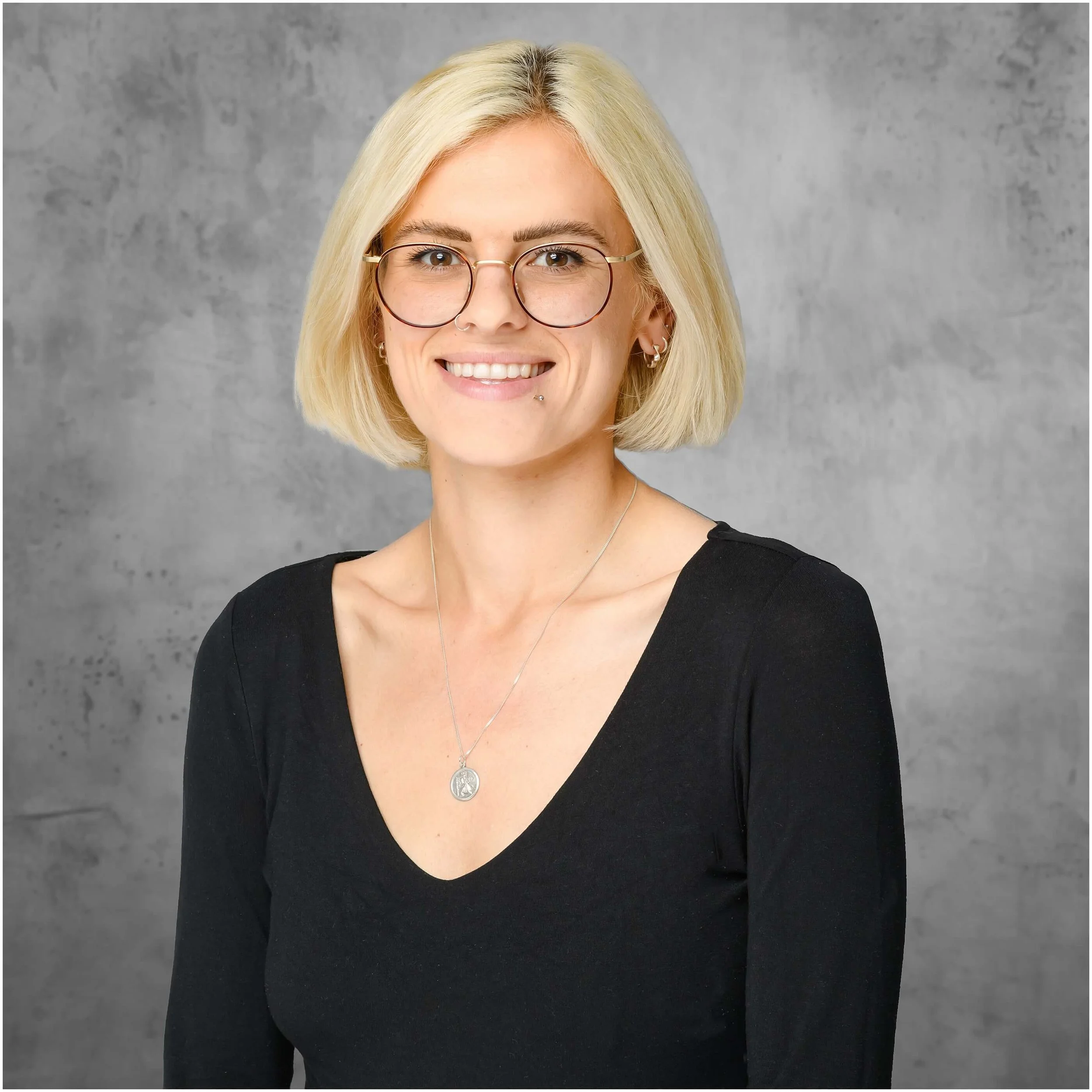 High quality creative headshot of a blonde woman standing in front of a concrete style background taken by Mick Cookson