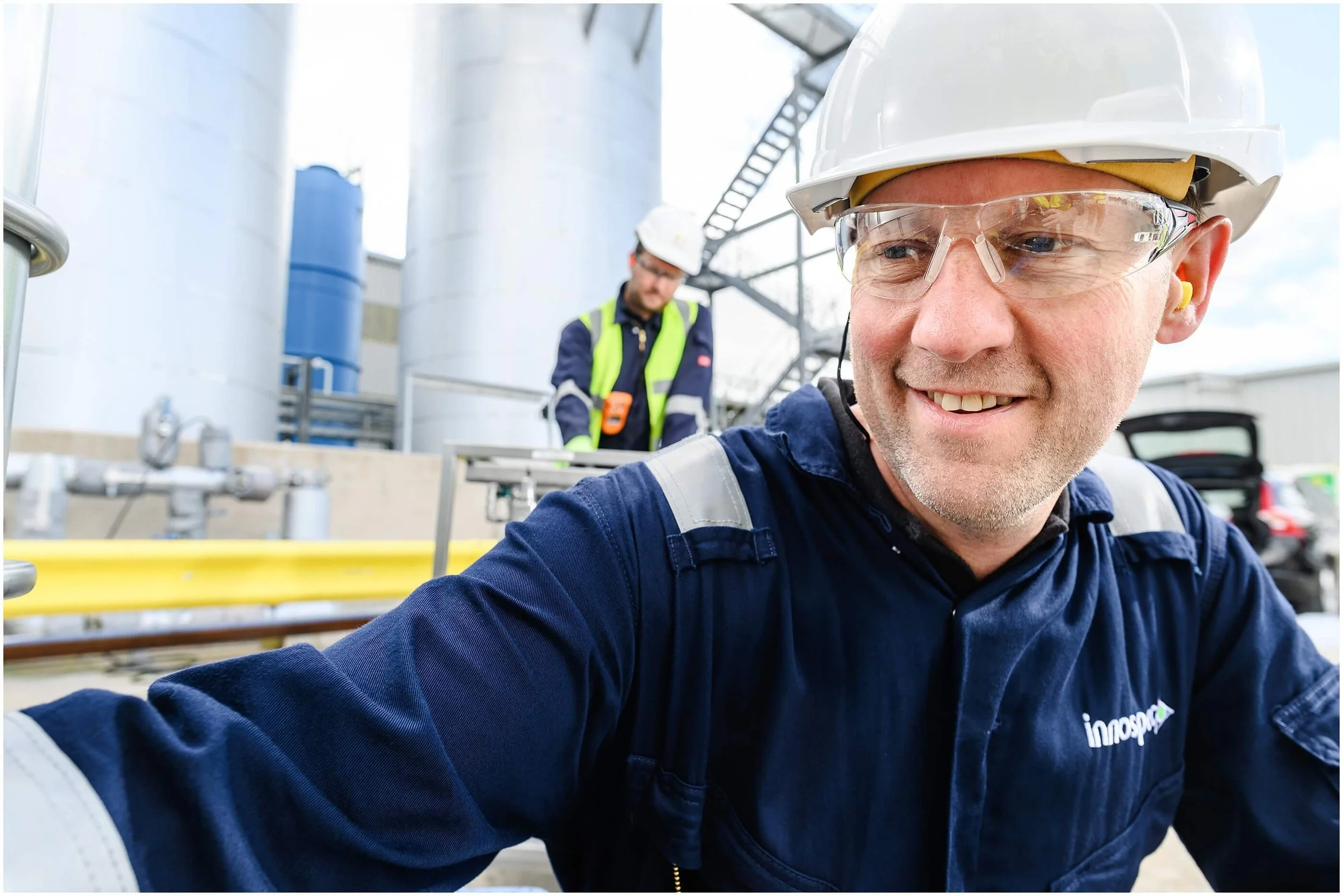 Smiling industrial worker in a hard hat and safety glasses at a manufacturing facility