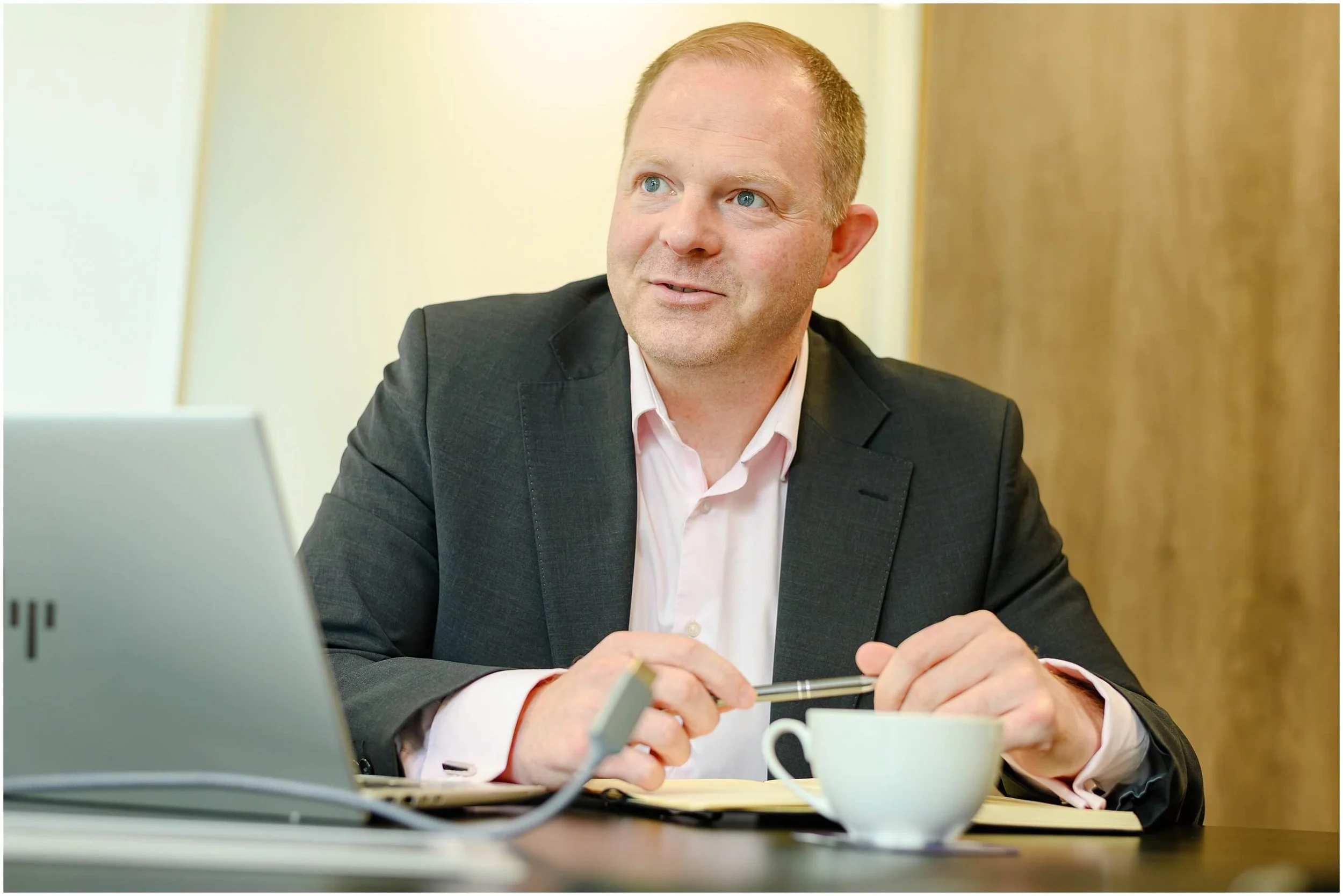 Businessman in a suit working at a laptop with a notebook and coffee cup