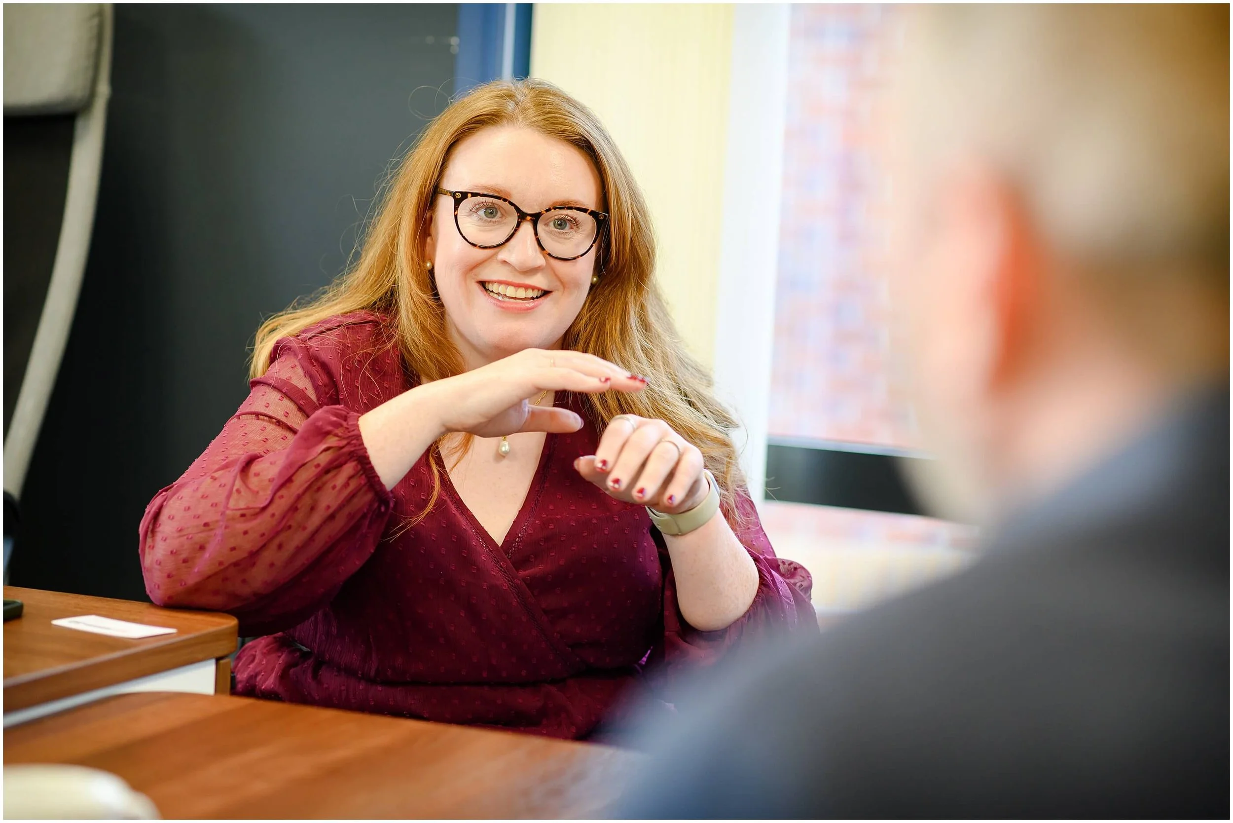 Smiling woman in glasses gesturing during a conversation at a table