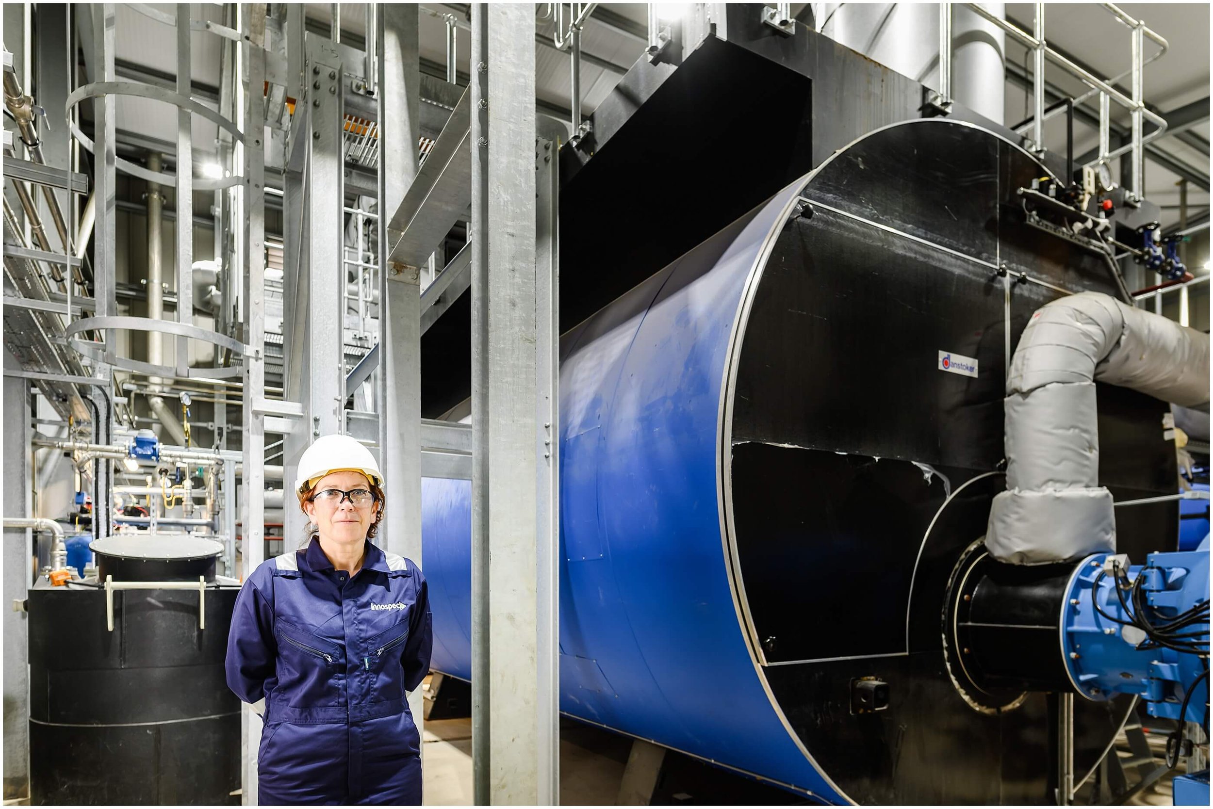 Industrial worker in safety gear standing beside large blue and black processing equipment in a manufacturing facility