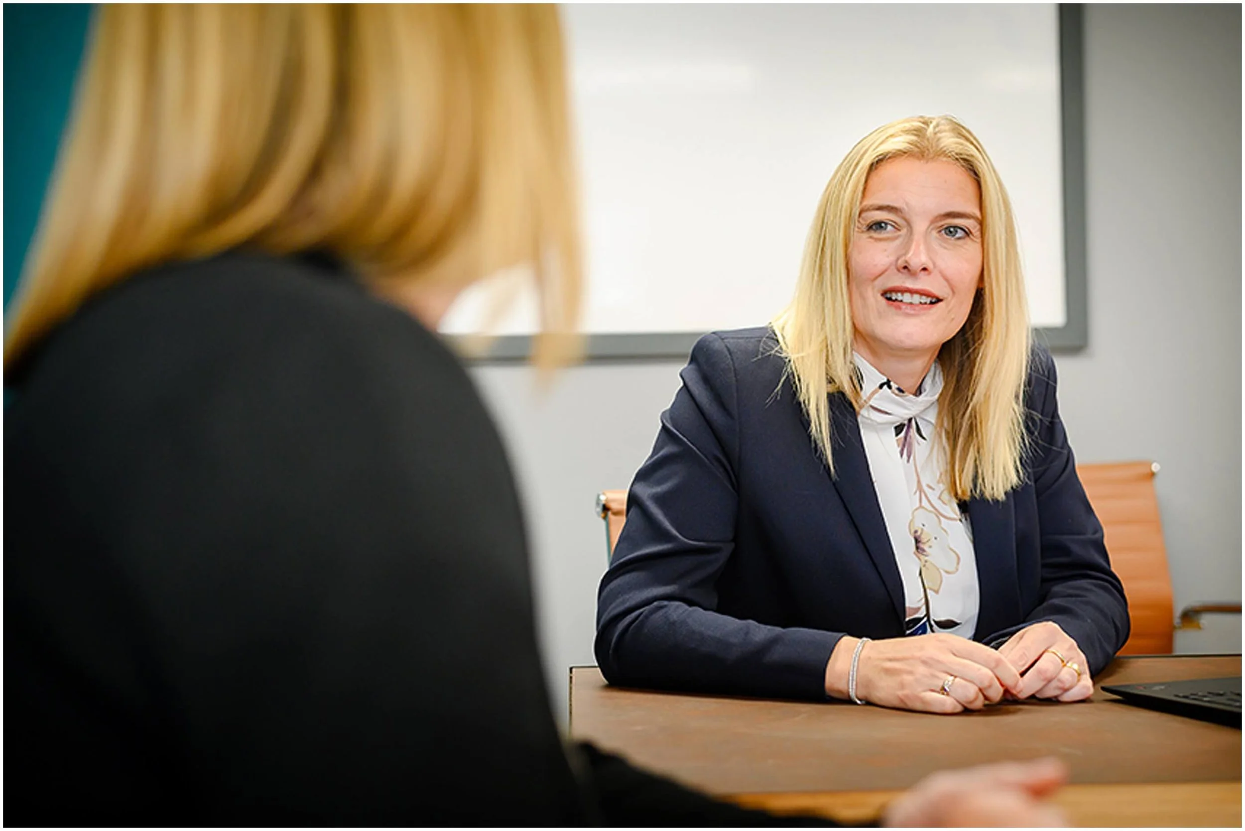 Businesswoman in a blazer speaking with a colleague across a conference table