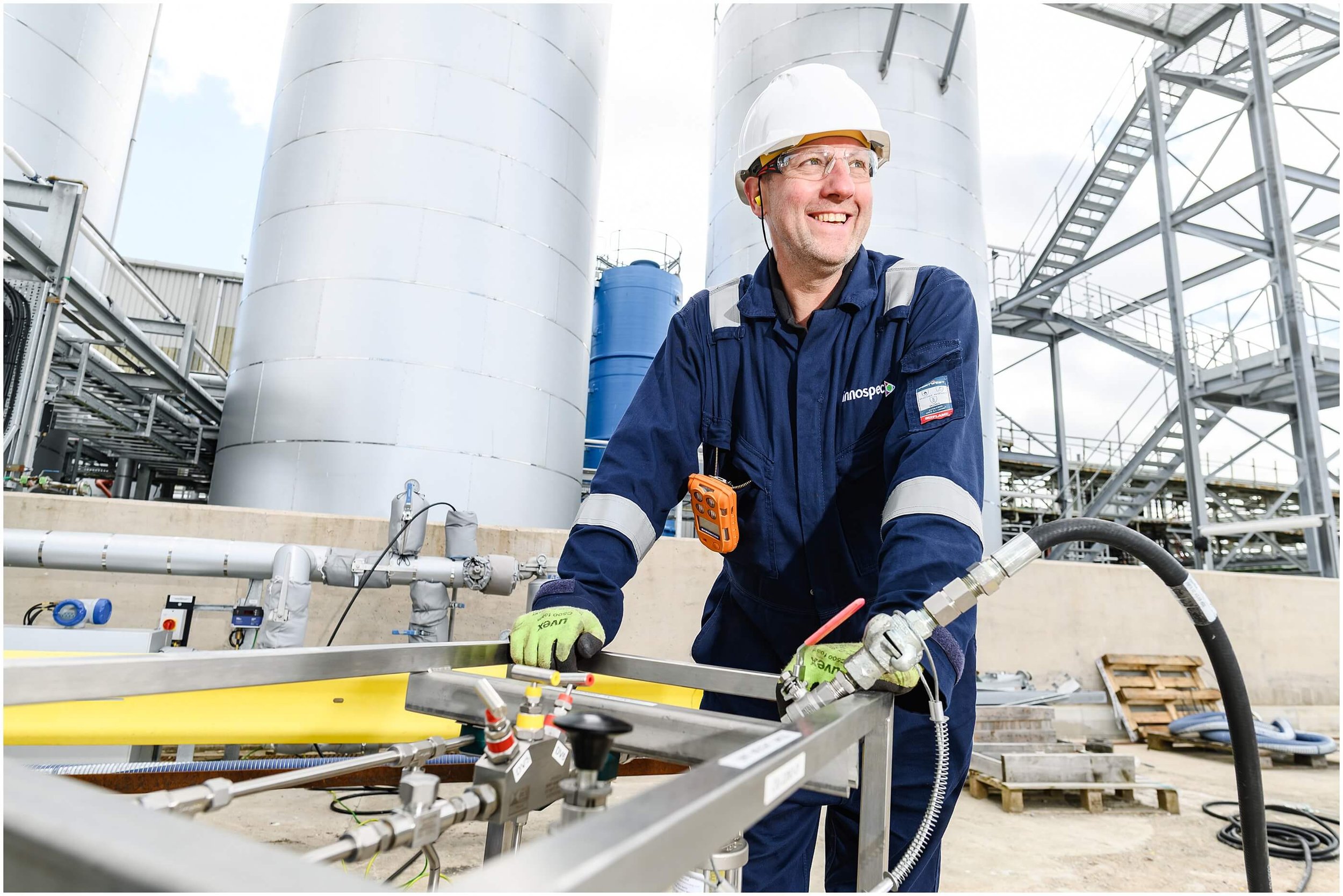 Industrial worker in protective gear operating equipment among large storage tanks and pipework