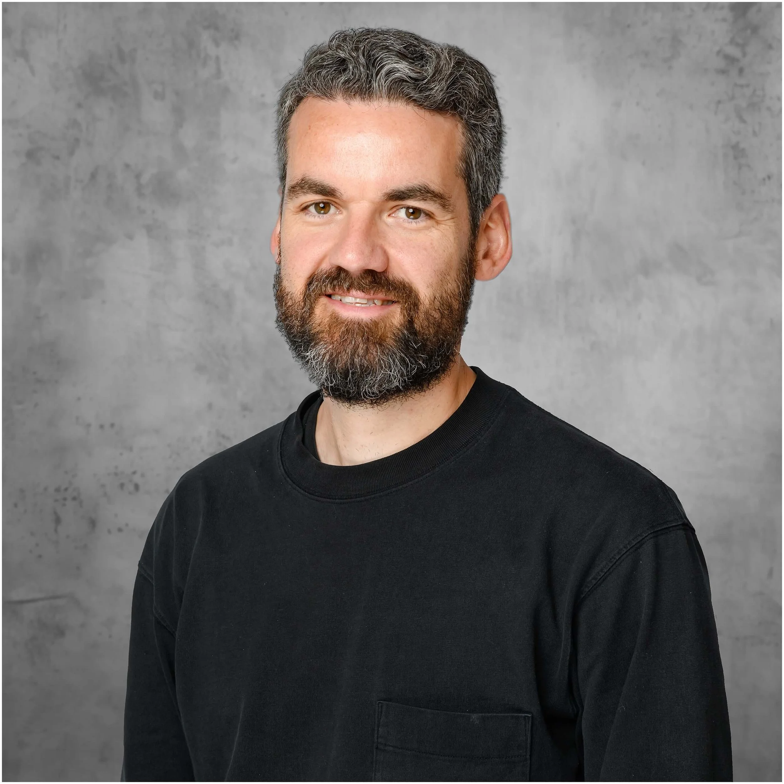 High quality creative headshot of a man with a beard standing in front of a concrete style background taken by Mick Cookson