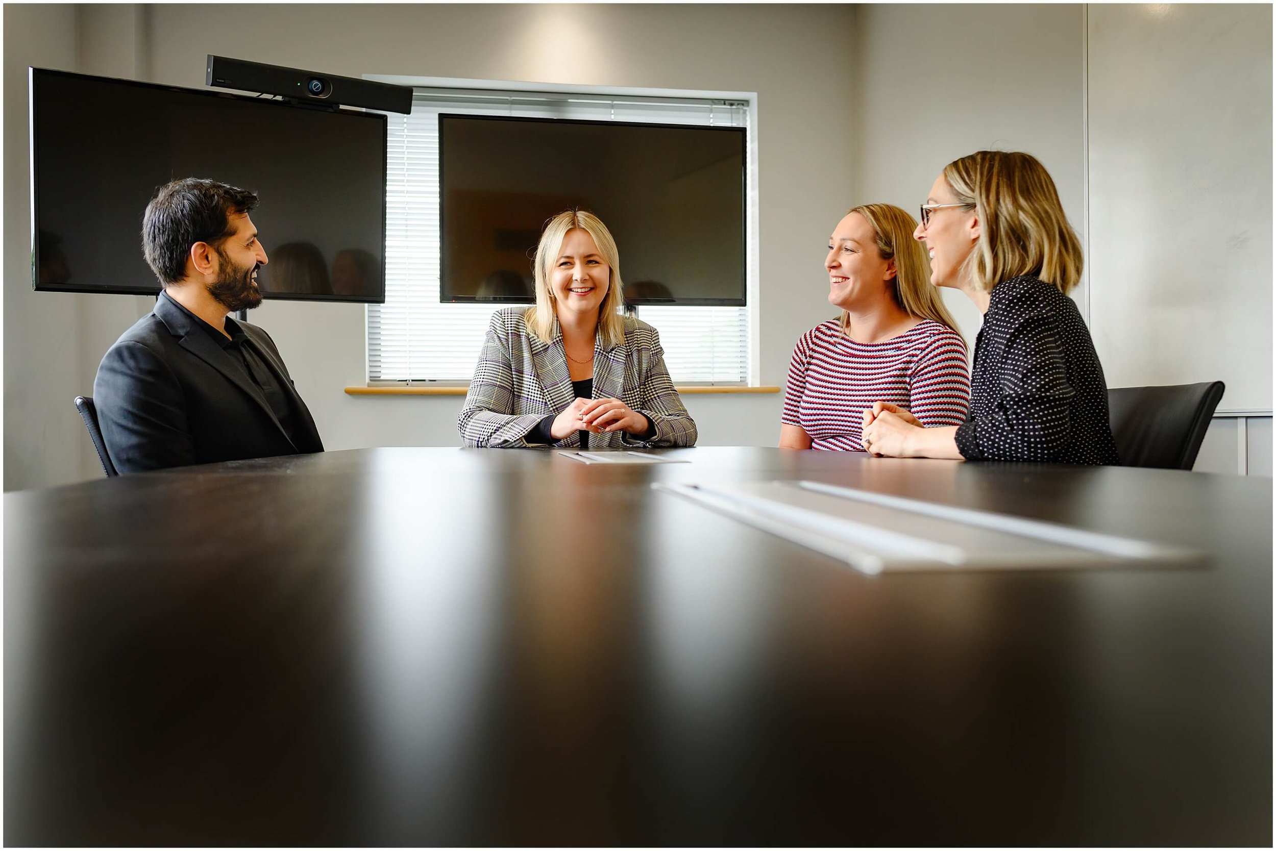 Four colleagues smiling and talking around a conference table in a modern office meeting room