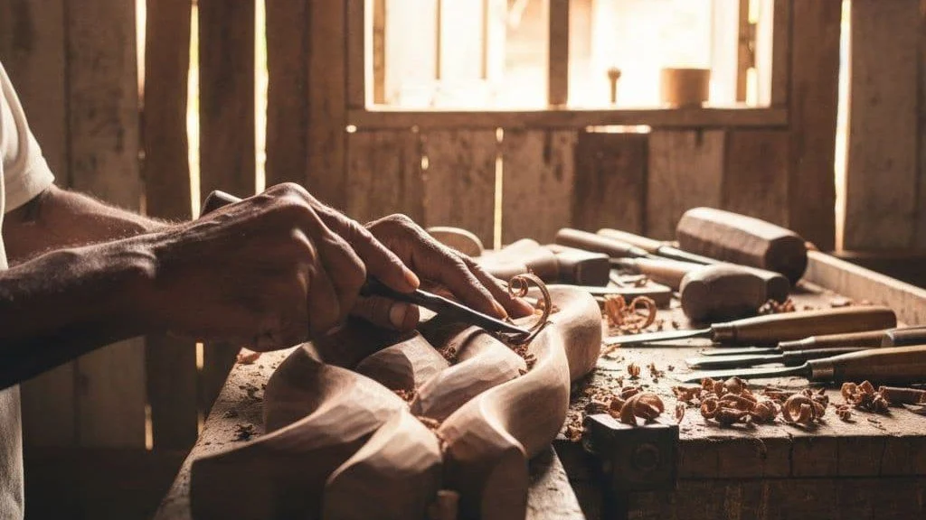 Close up of an artisan's hands carving wood with traditional tools in a rustic workshop.