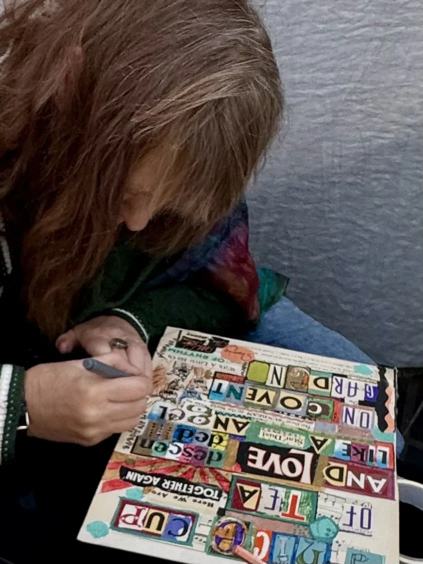 Artist signing a colorful mixed-media print at a table.