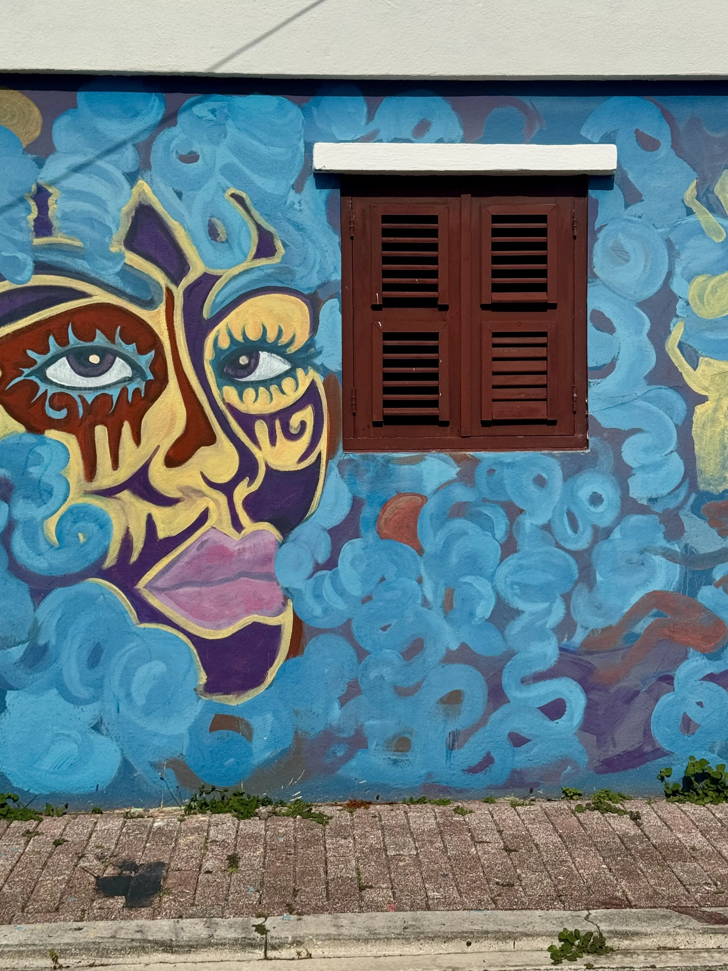 Colorful face mural beside red shuttered window in Curaçao street art district